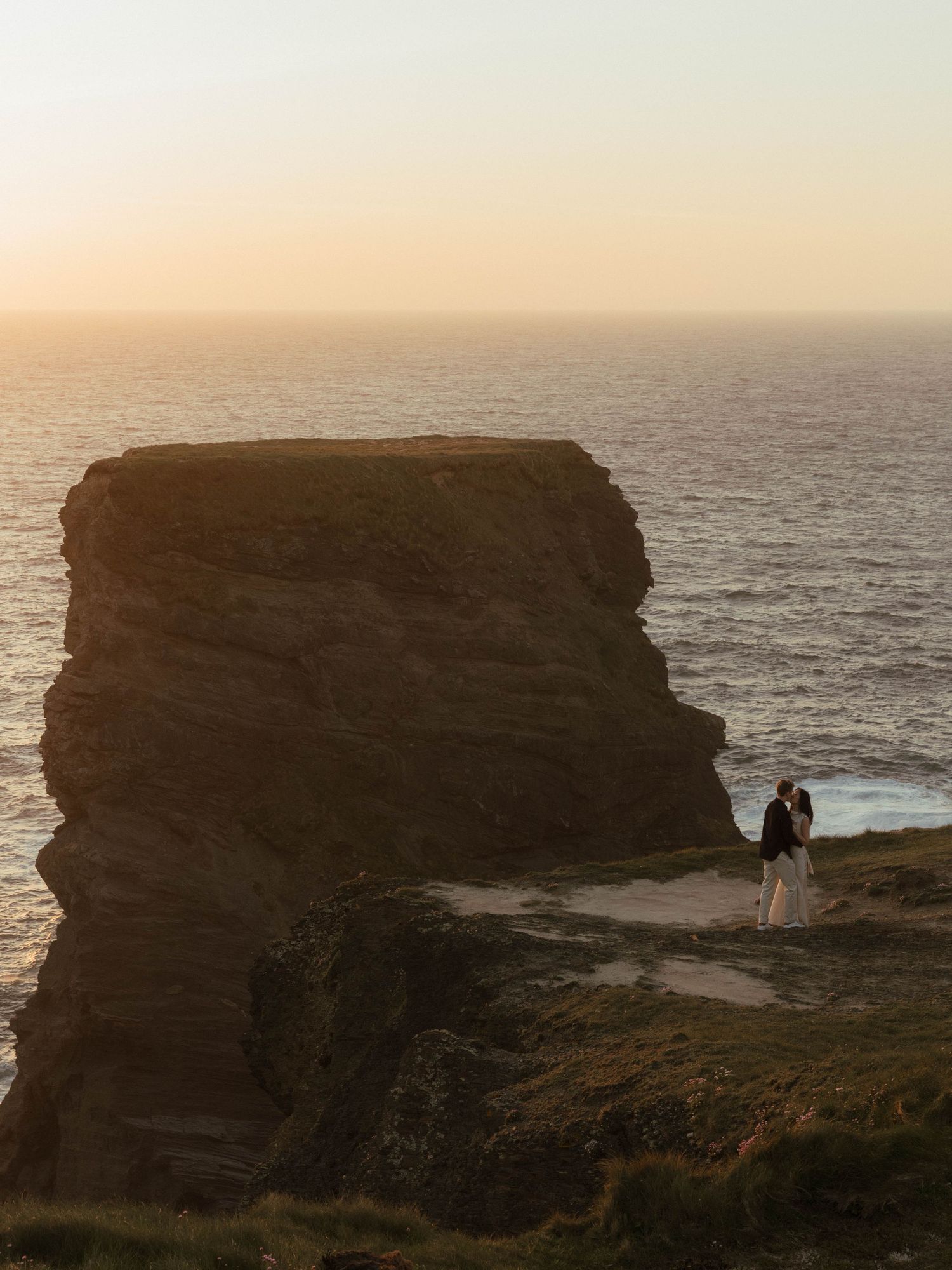Dramatic coastal cliffs overlooking the ocean at sunset with silhouettes against the horizon.