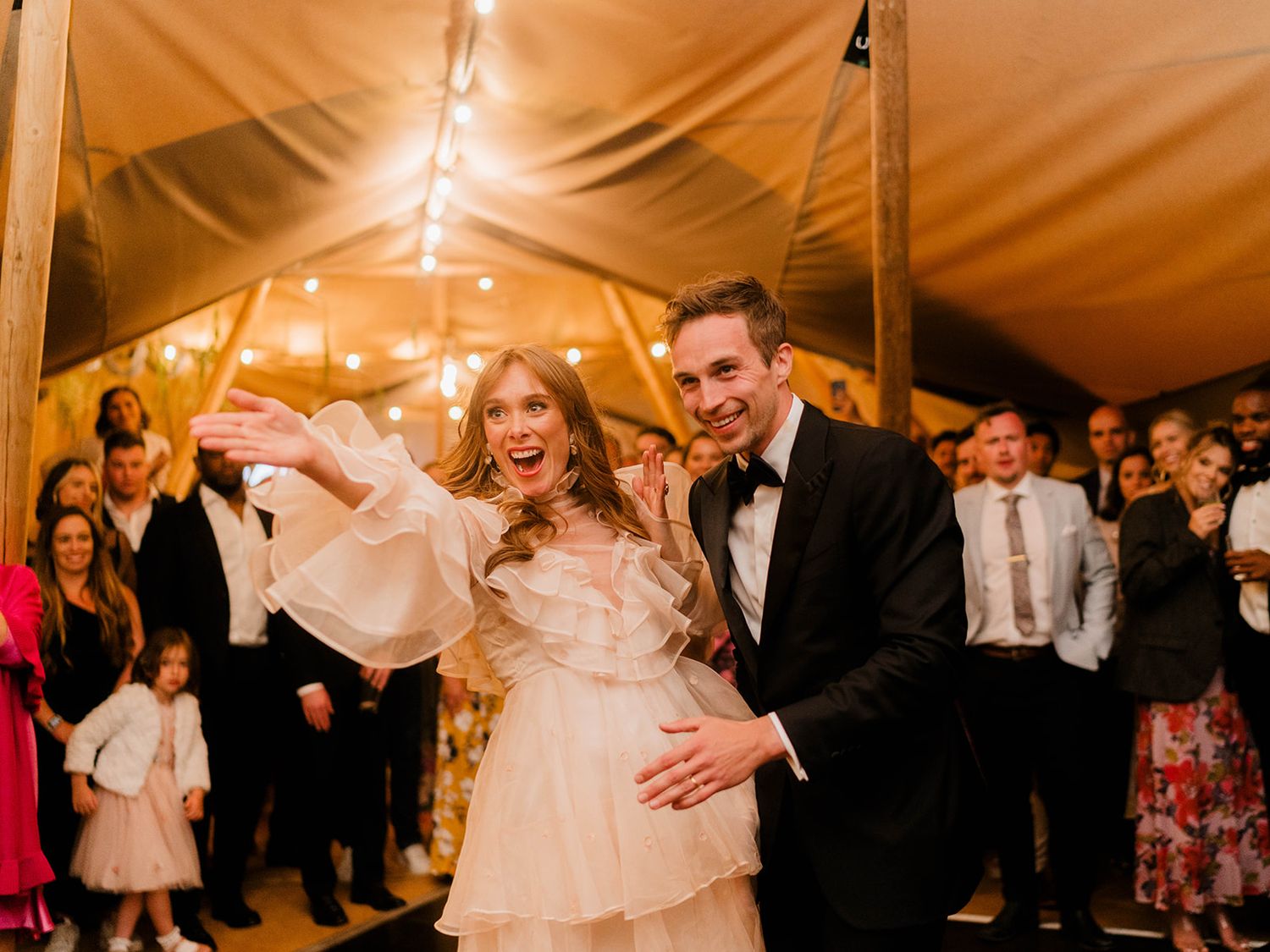 A couple shares their first dance at a wedding reception under warm lighting in an elegant tent venue.
