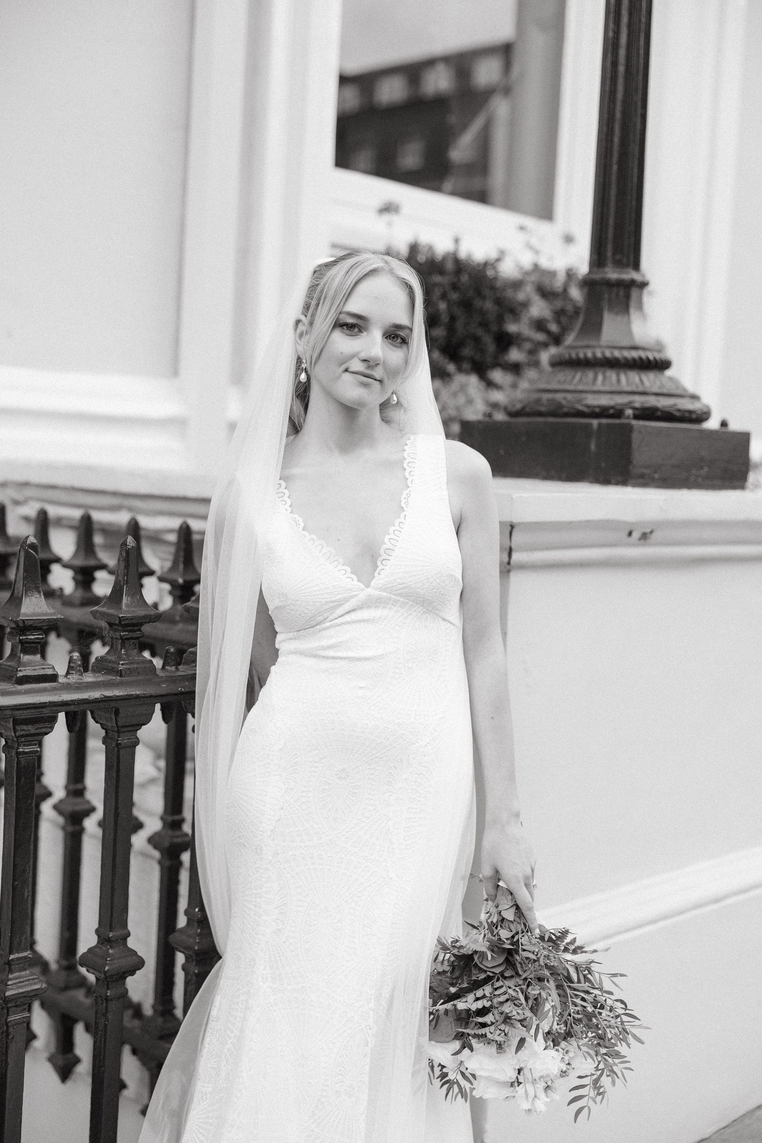 A bride in an elegant white v-neck wedding dress poses on historic stone steps with a natural bouquet.