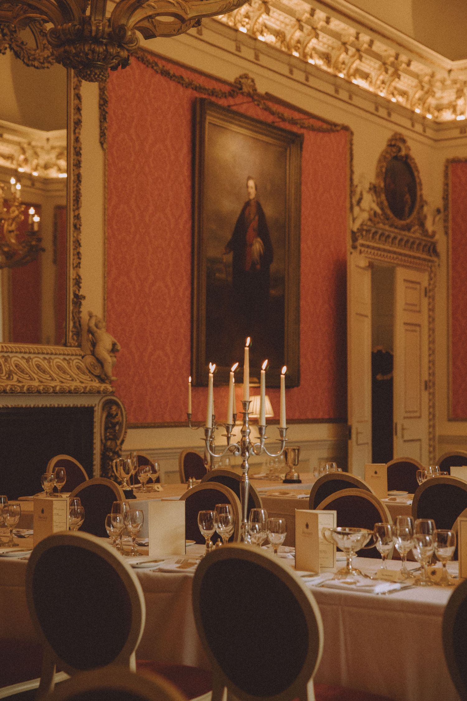 Elegant dining room with ornate decor featuring white tablecloths, candelabras, and red damask wallpaper in a historic setting.