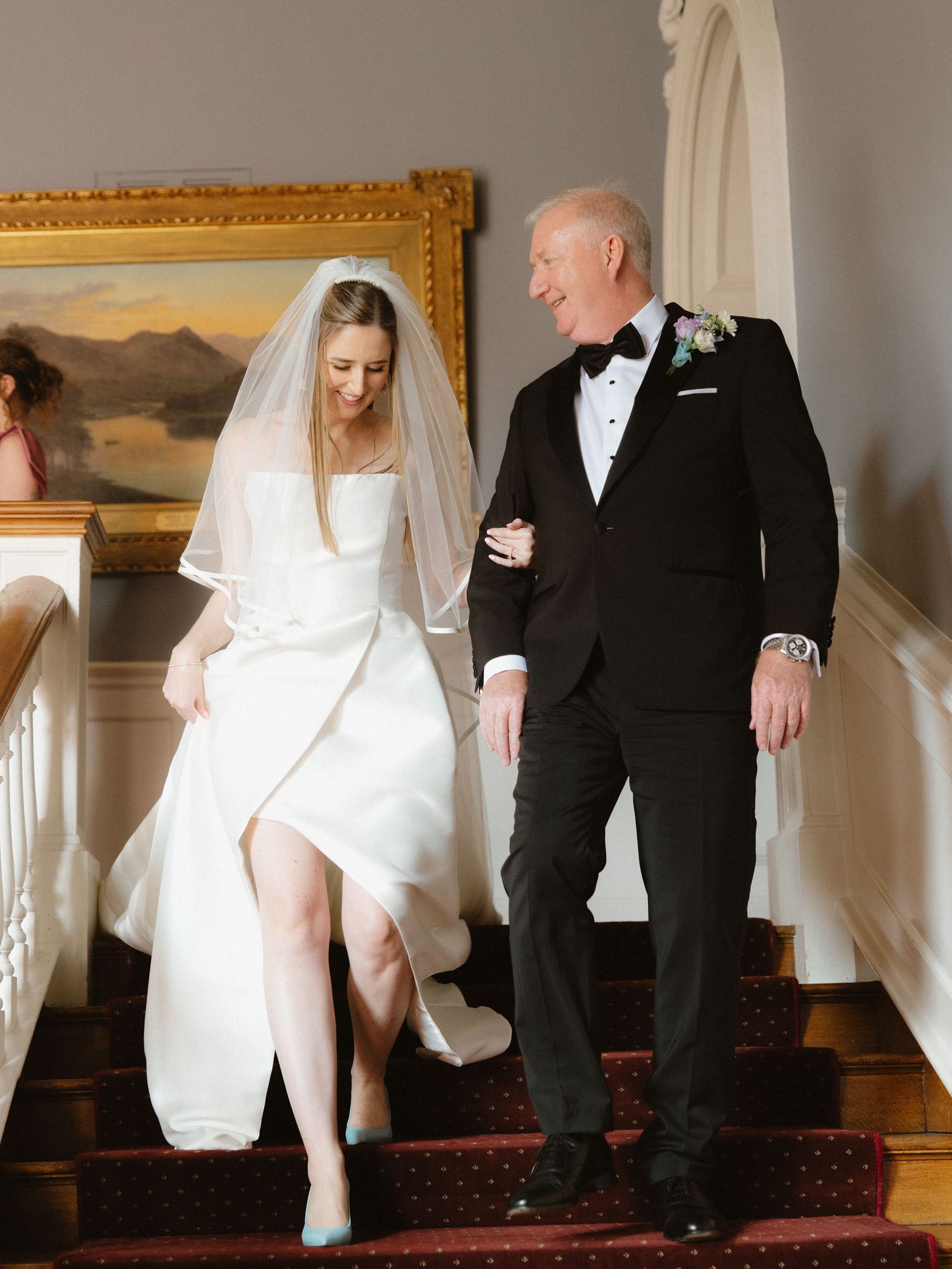 A pair walking down elegant stairs in formal wedding attire.
