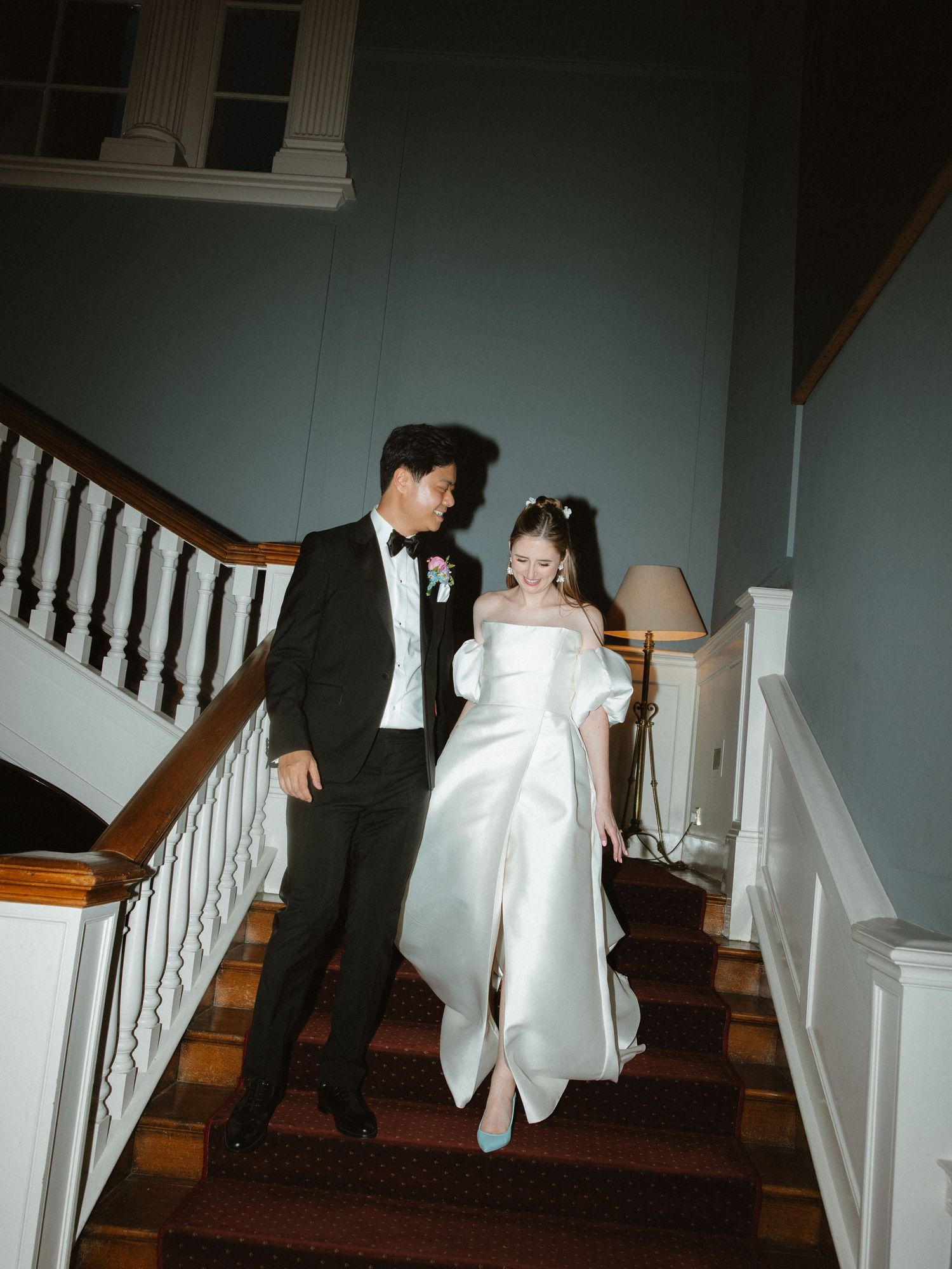 Wedding couple descending vintage staircase in formal attire.