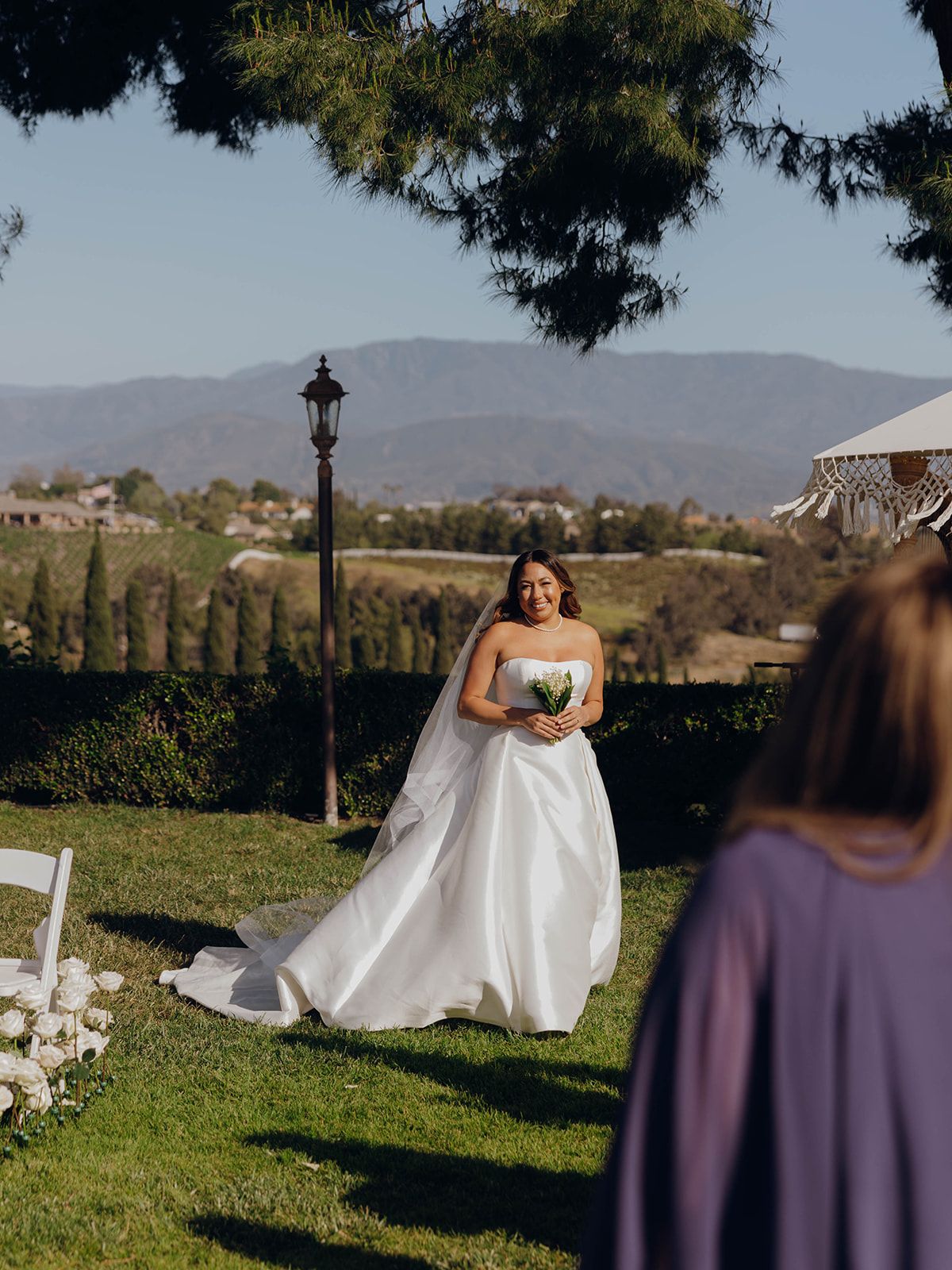 Outdoor wedding ceremony at a scenic vineyard estate with rolling hills and mountains in the background.