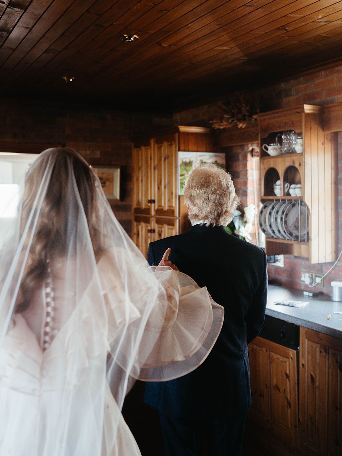 A wedding day moment captured in a rustic wooden kitchen with natural lighting.