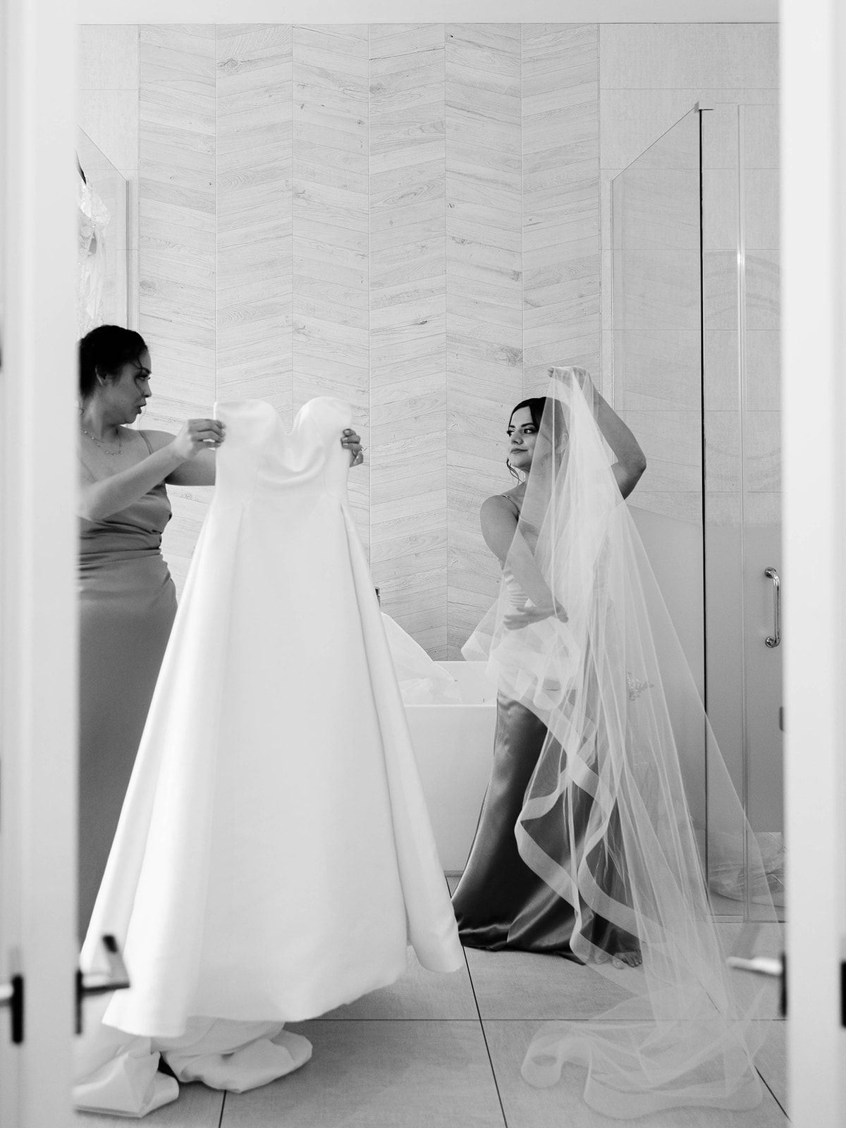 A bride in her white wedding dress and veil gets ready for her special day in a dressing room.