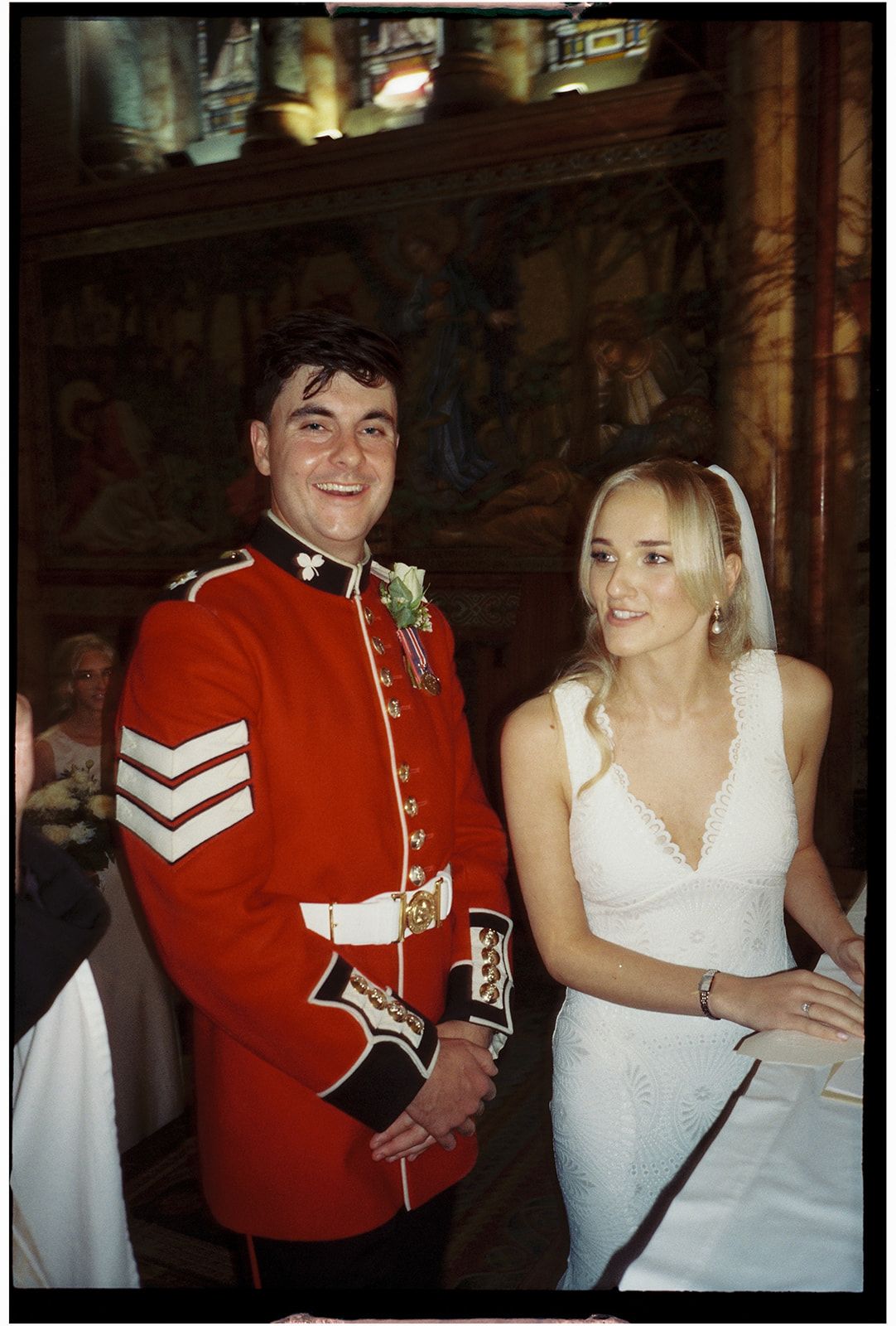 A wedding photo showing a person in a formal red military uniform with sergeant stripes next to someone in a white dress.
