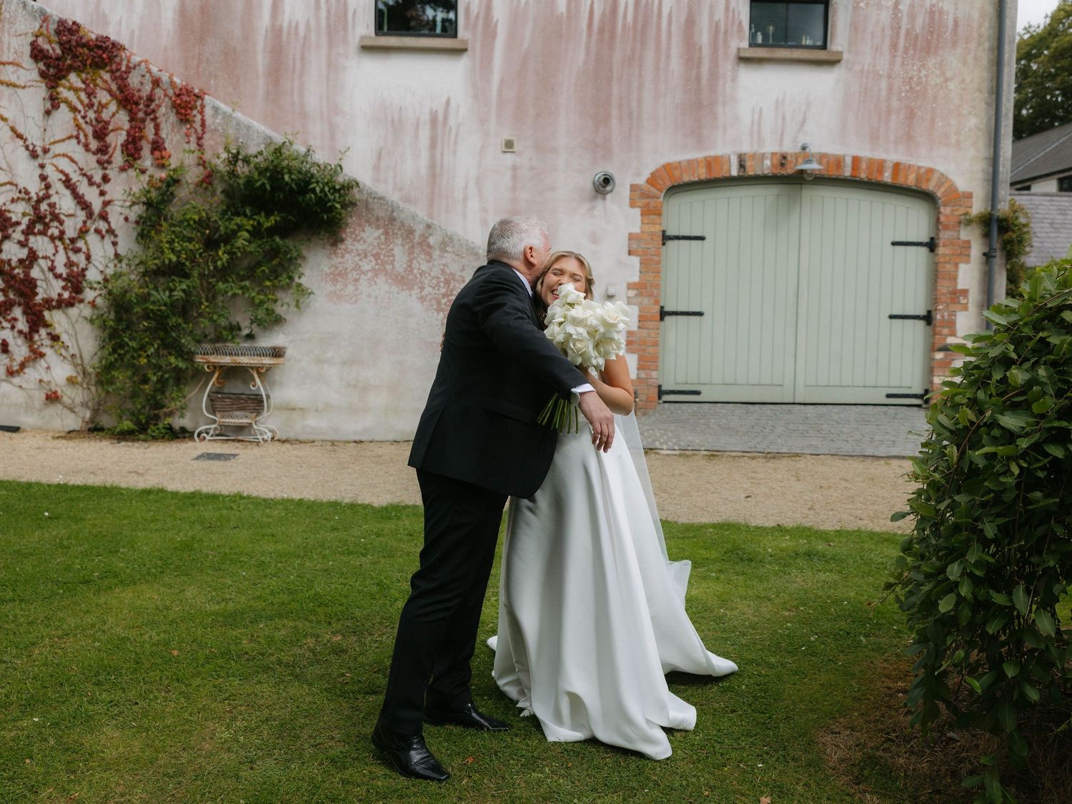 Emotional embrace between bride and father outside vintage building.