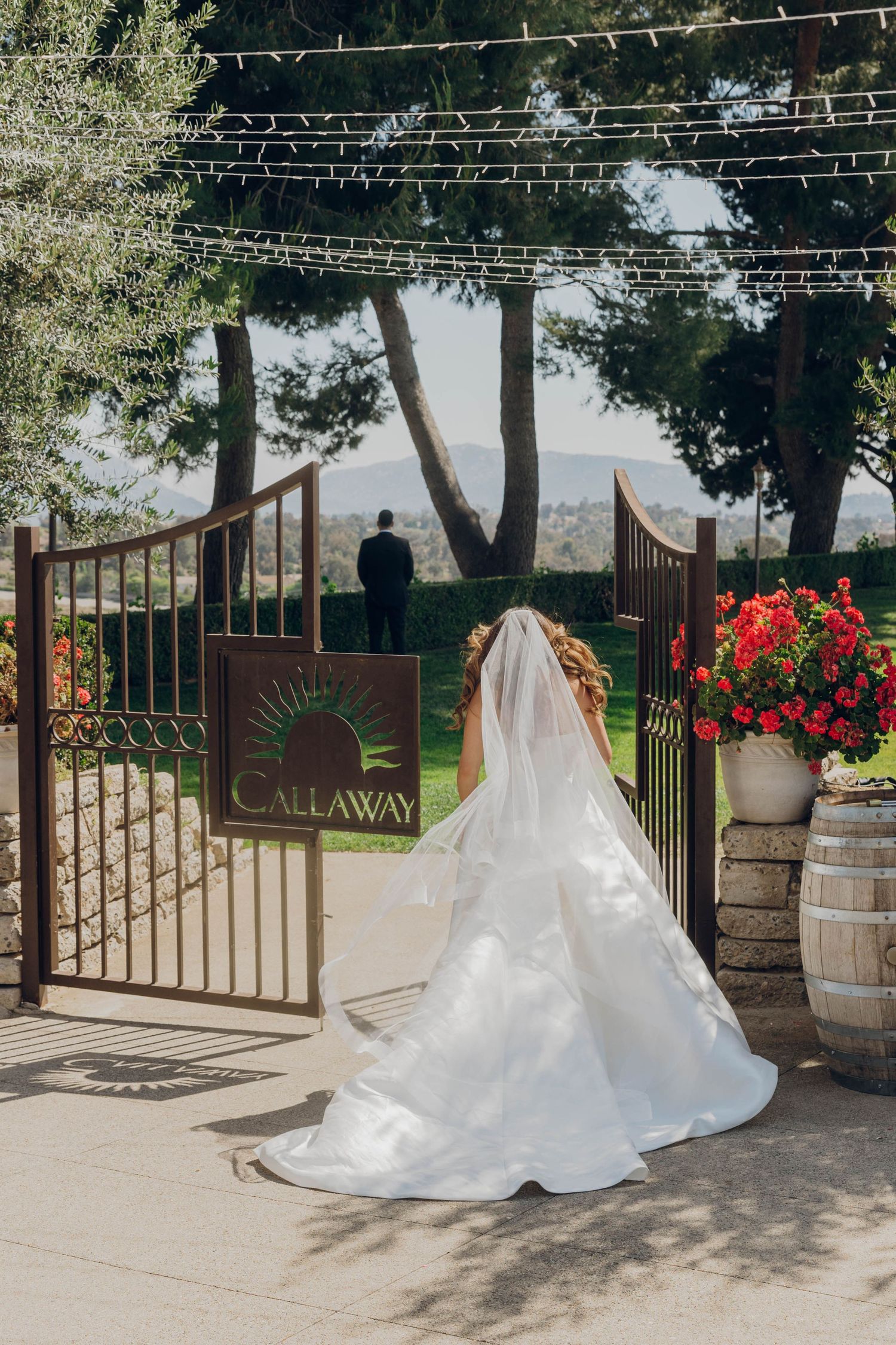 A flowing white wedding dress train elegantly trails across the ground in front of an ornate iron gate entrance.