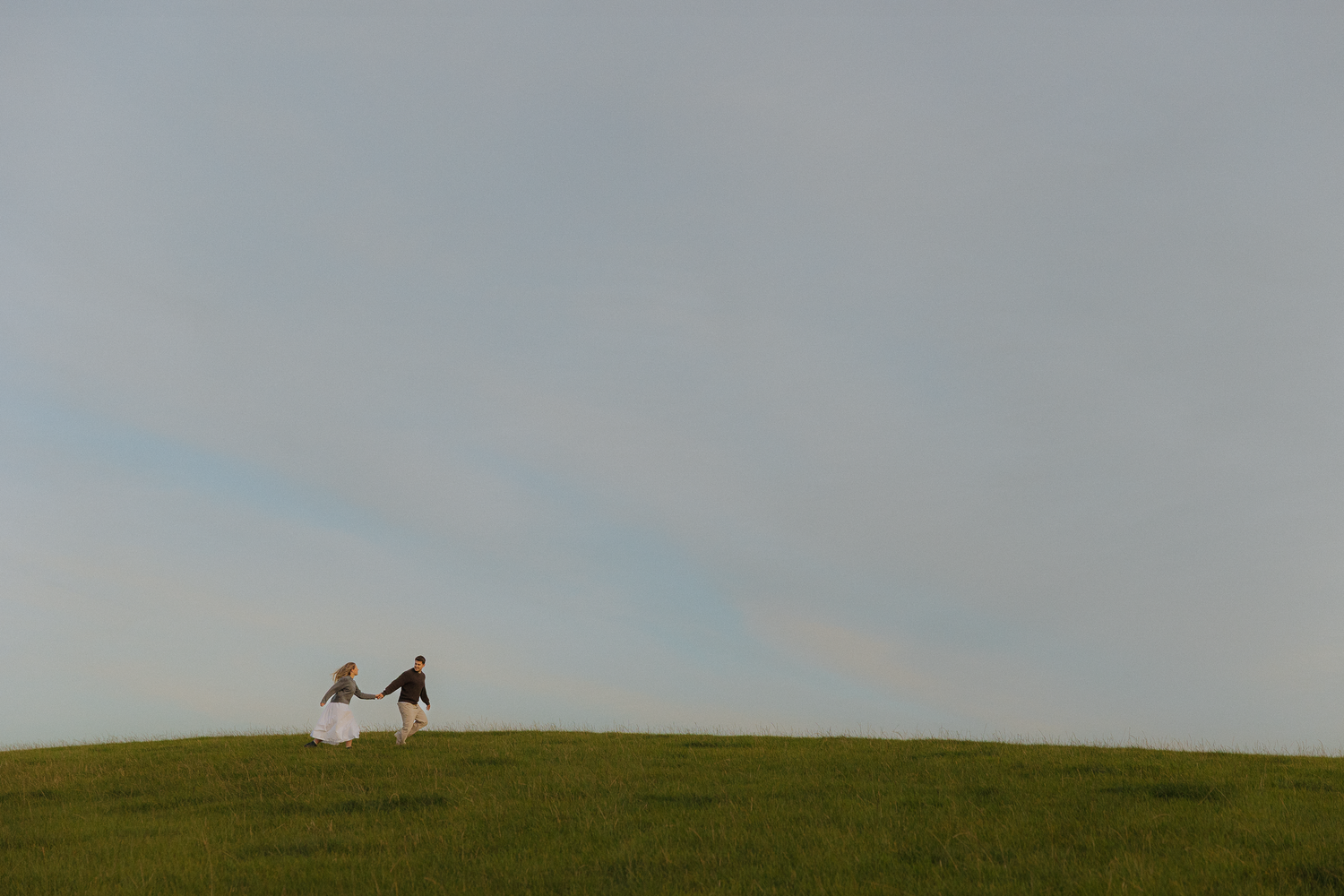 Two silhouettes walk along a hilltop horizon against a bright sky.