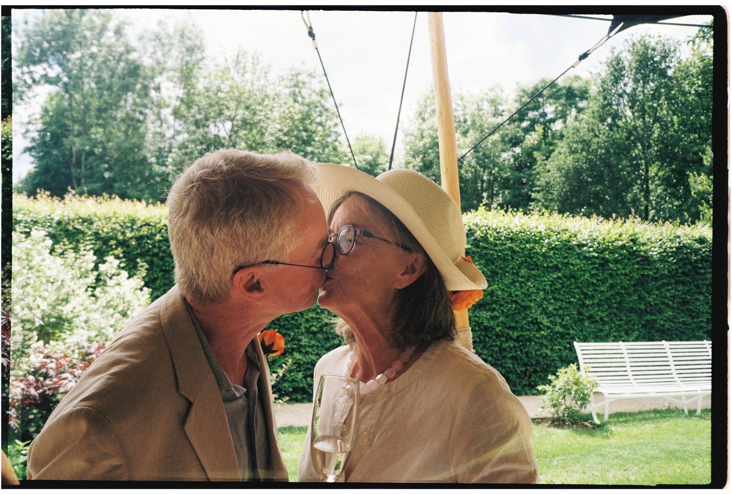 Older couple sharing a romantic kiss outdoors in a garden setting during a wedding celebration.