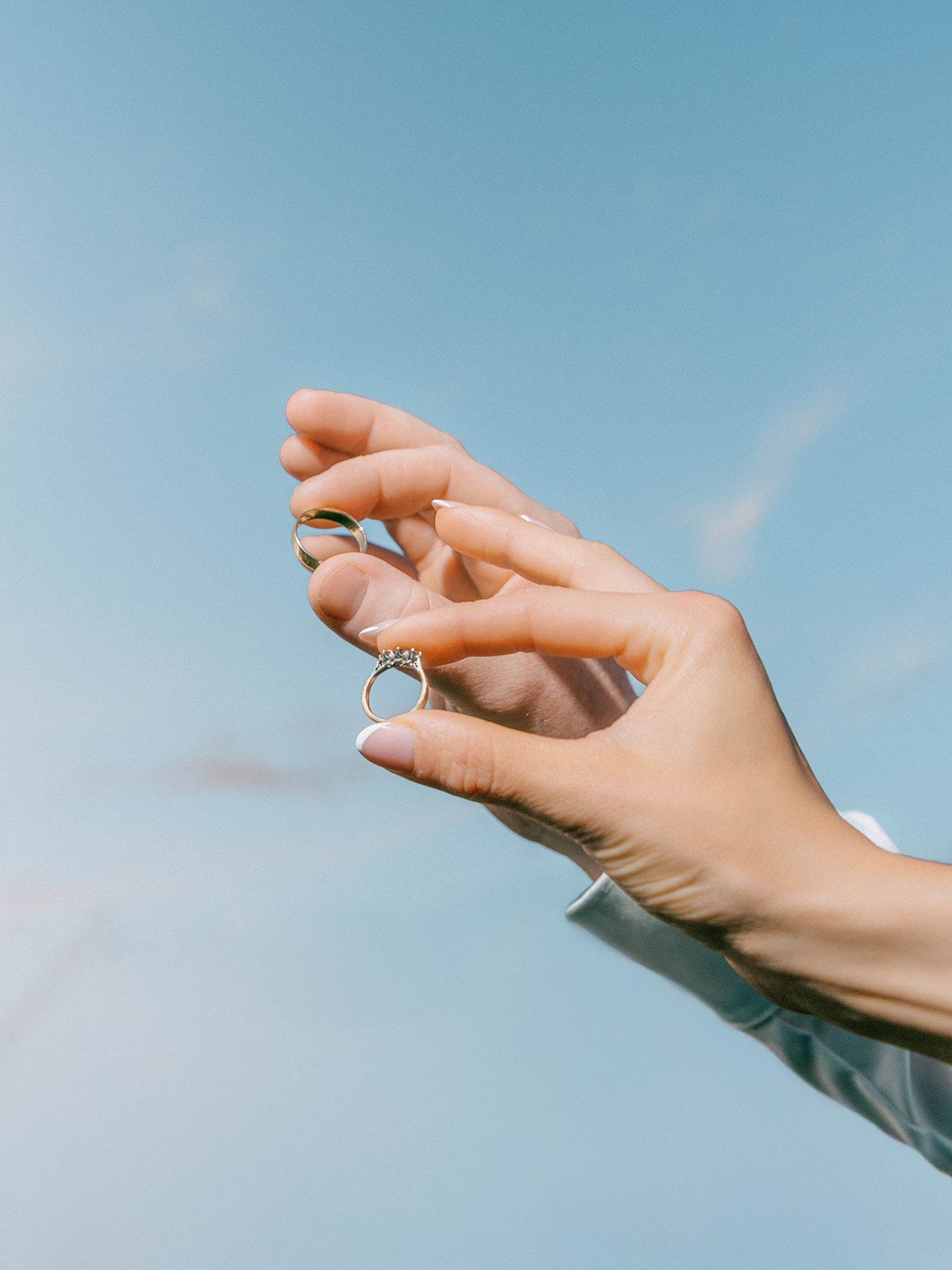 A delicate hand reaches toward a blue sky while wearing multiple silver rings.