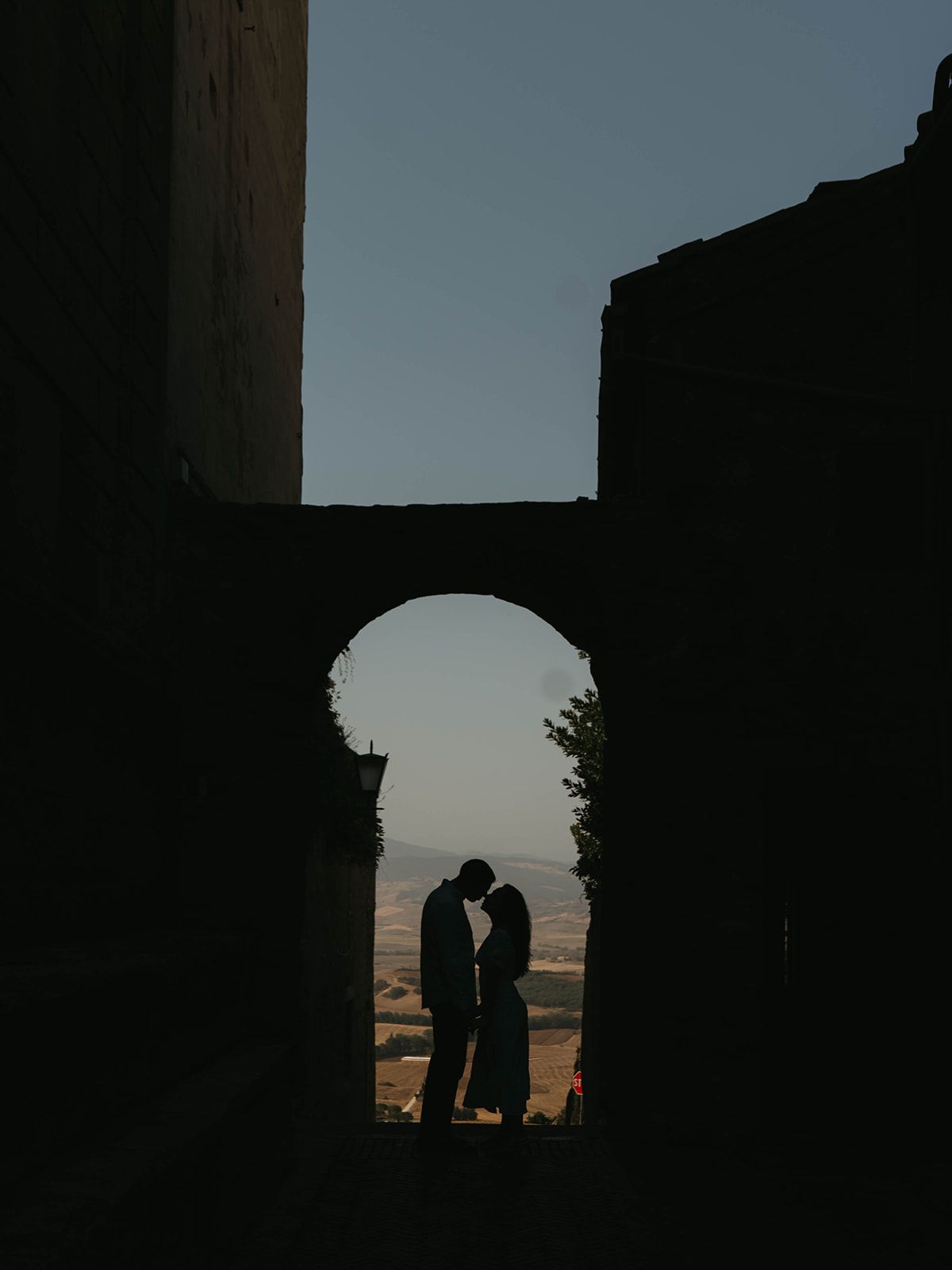 Silhouettes of a couple framed by ancient stone archway at sunset.