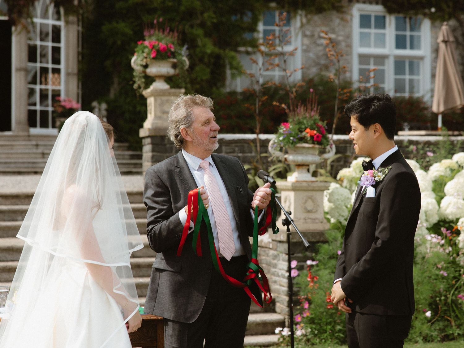 Wedding ceremony takes place on elegant stone steps with floral arrangements and classical architecture.