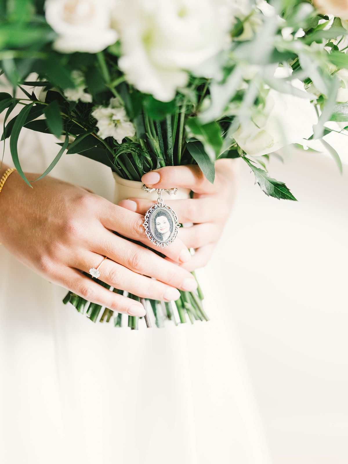 Hands holding white flower bouquet with large vintage-style statement ring and wedding band.