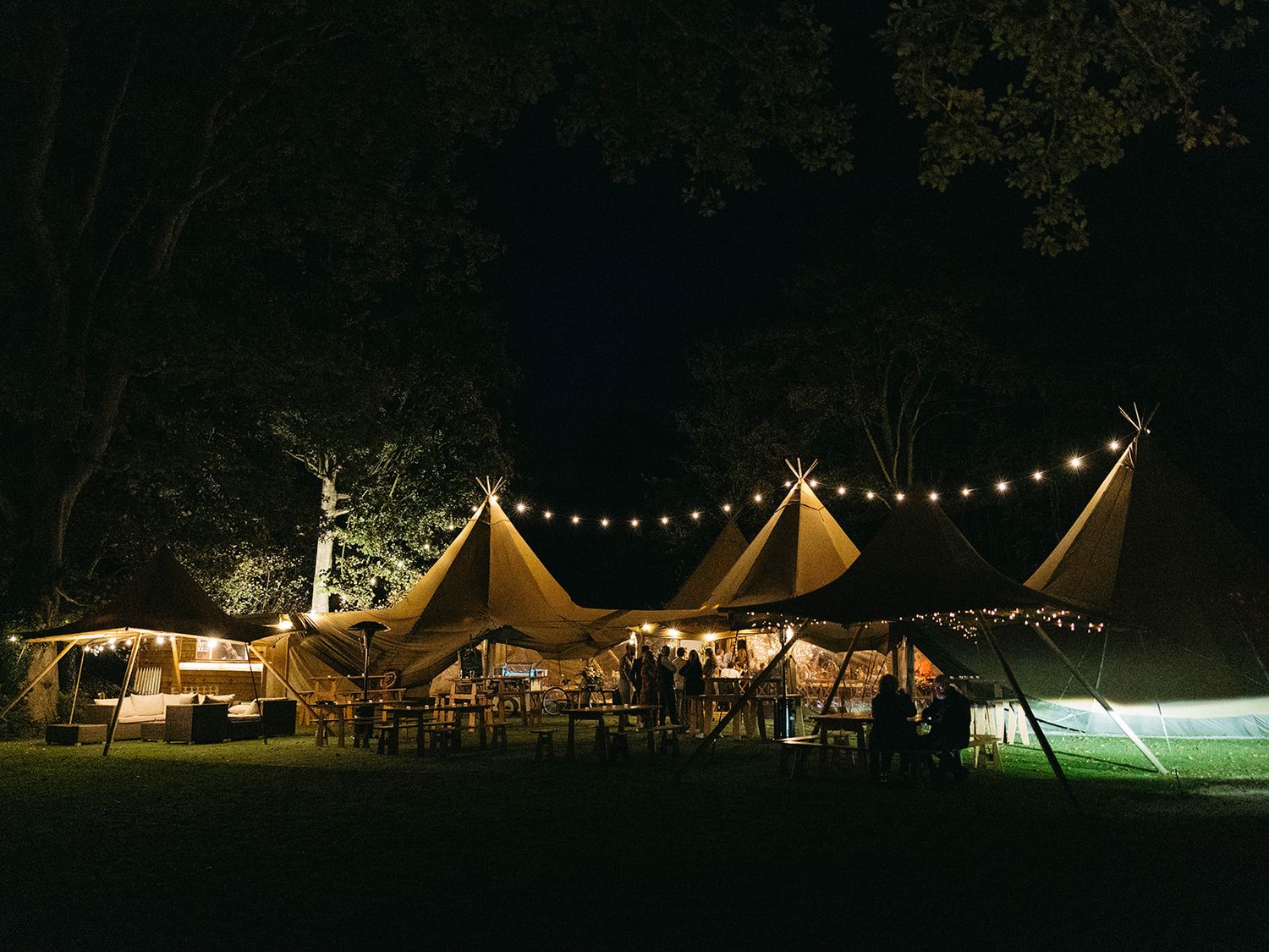 An illuminated outdoor wedding tent with string lights glowing warmly against the dark night sky at a festive event.