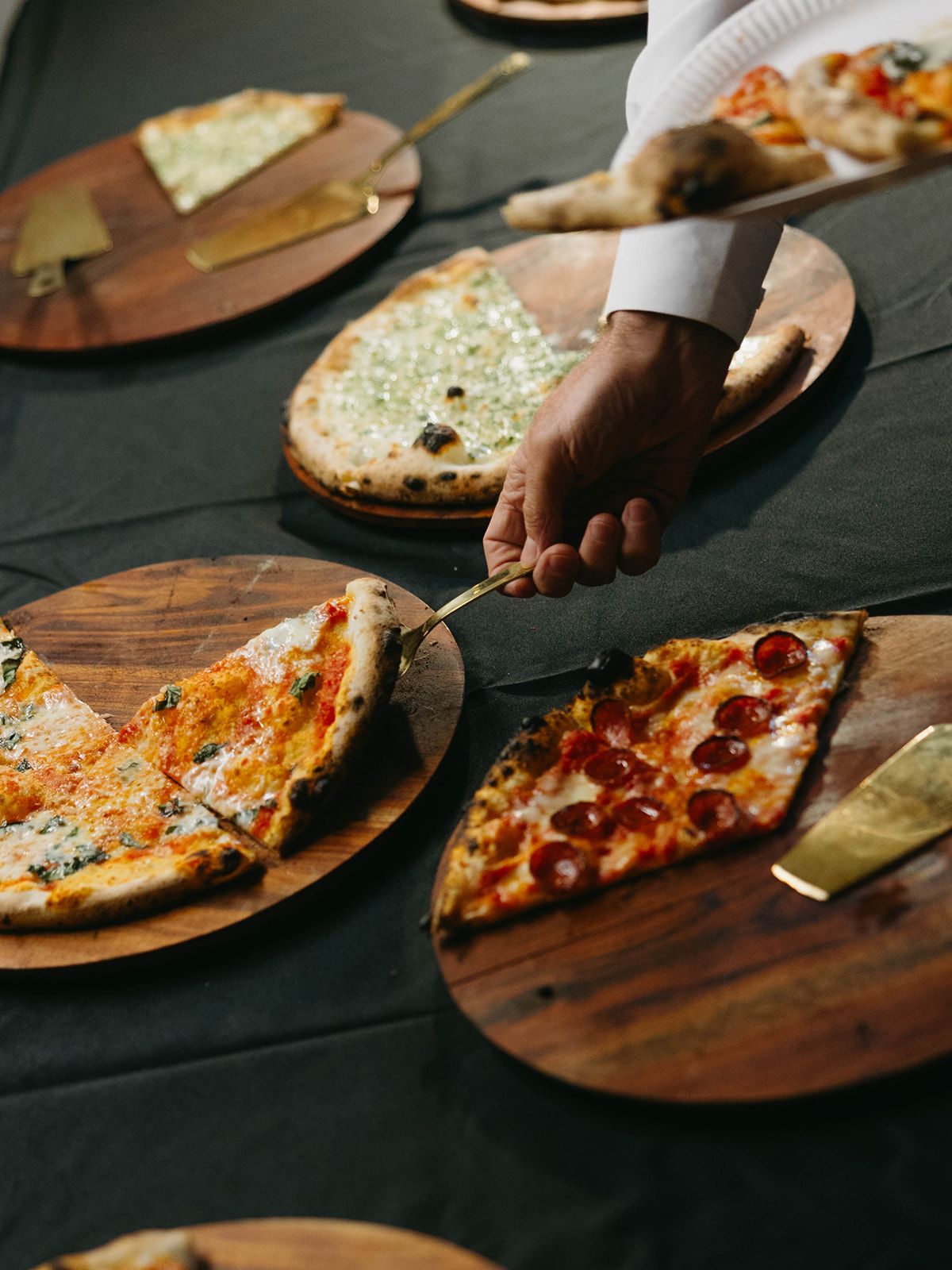 Various artisanal pizzas with different toppings served on wooden boards against a dark tablecloth at a gathering.