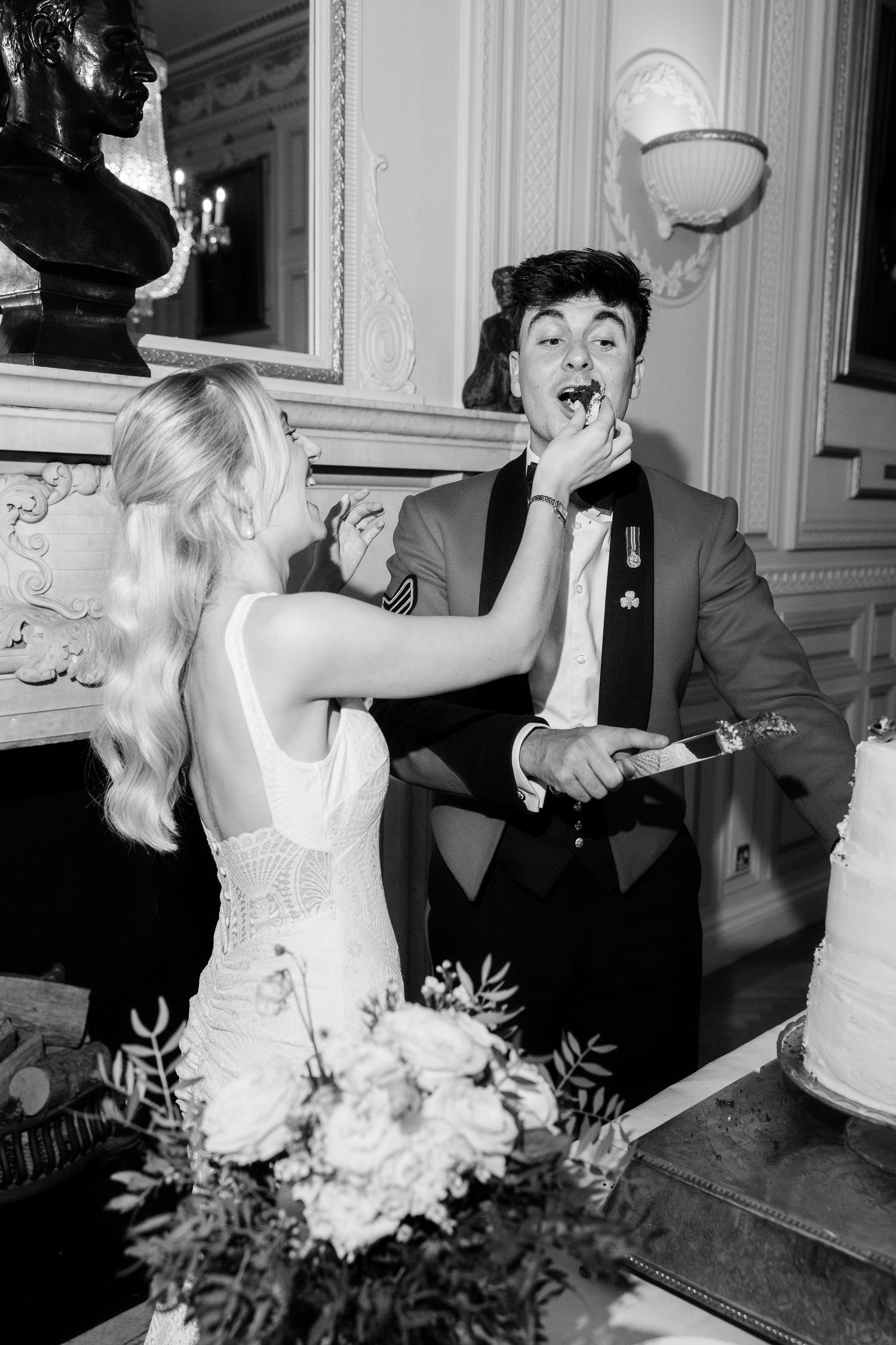 A joyful celebration captured in black and white as couple shares cake-cutting moment at their wedding reception.