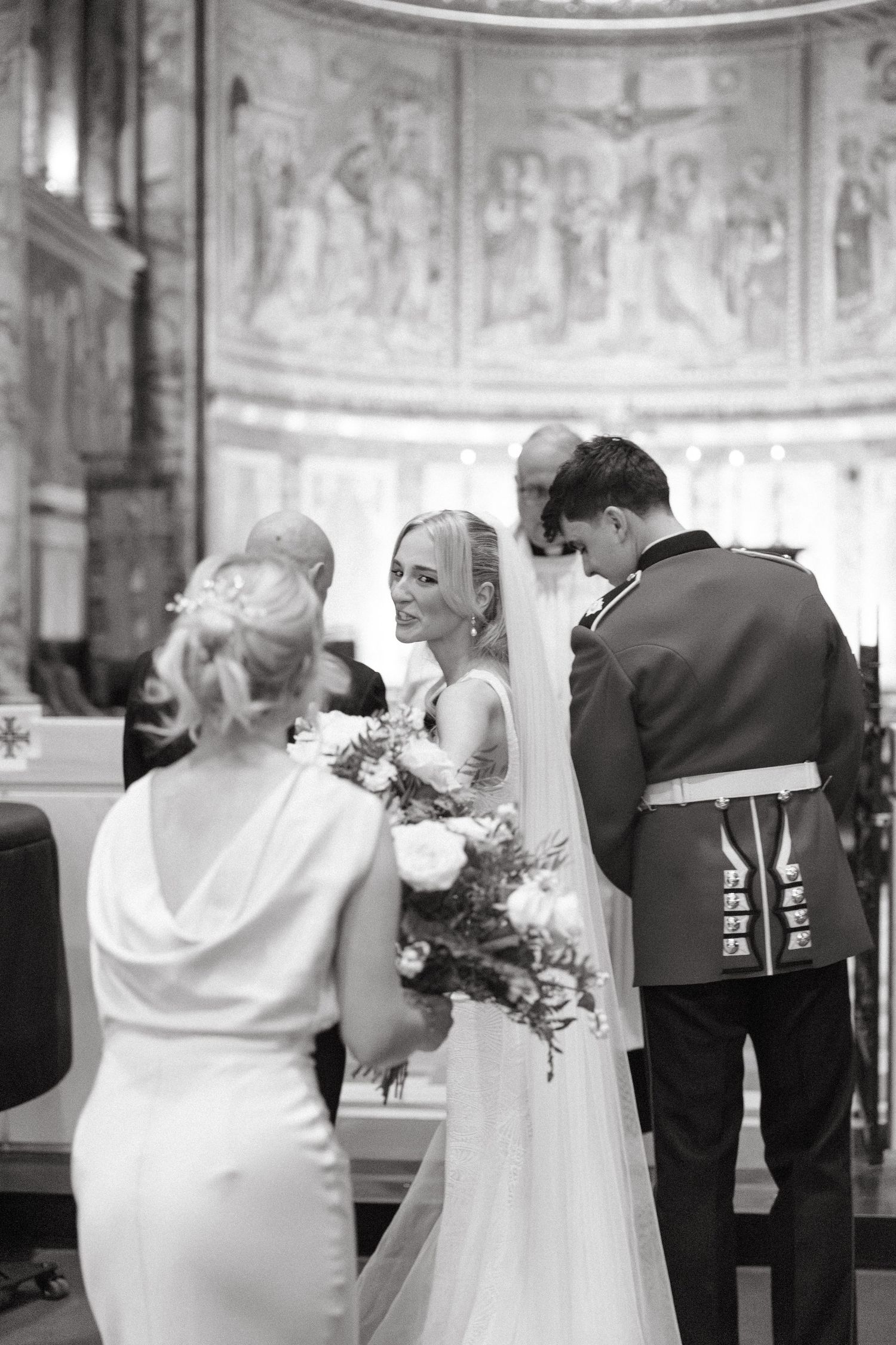 Black and white photo of a wedding ceremony in an elegant church interior showing guests and the wedding party.