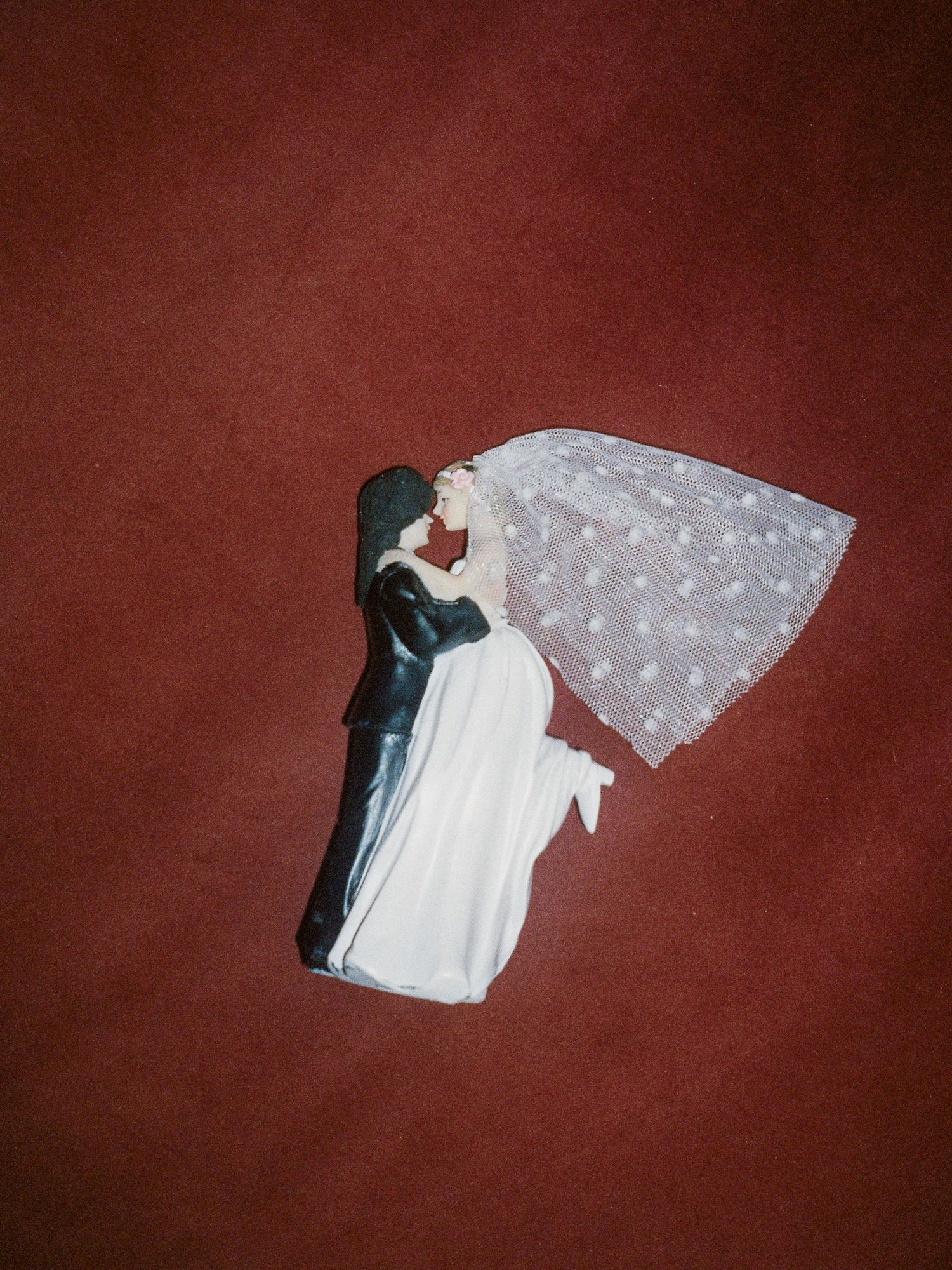 A sequence of four images showing a white veil with floral details falling against a dark red background.