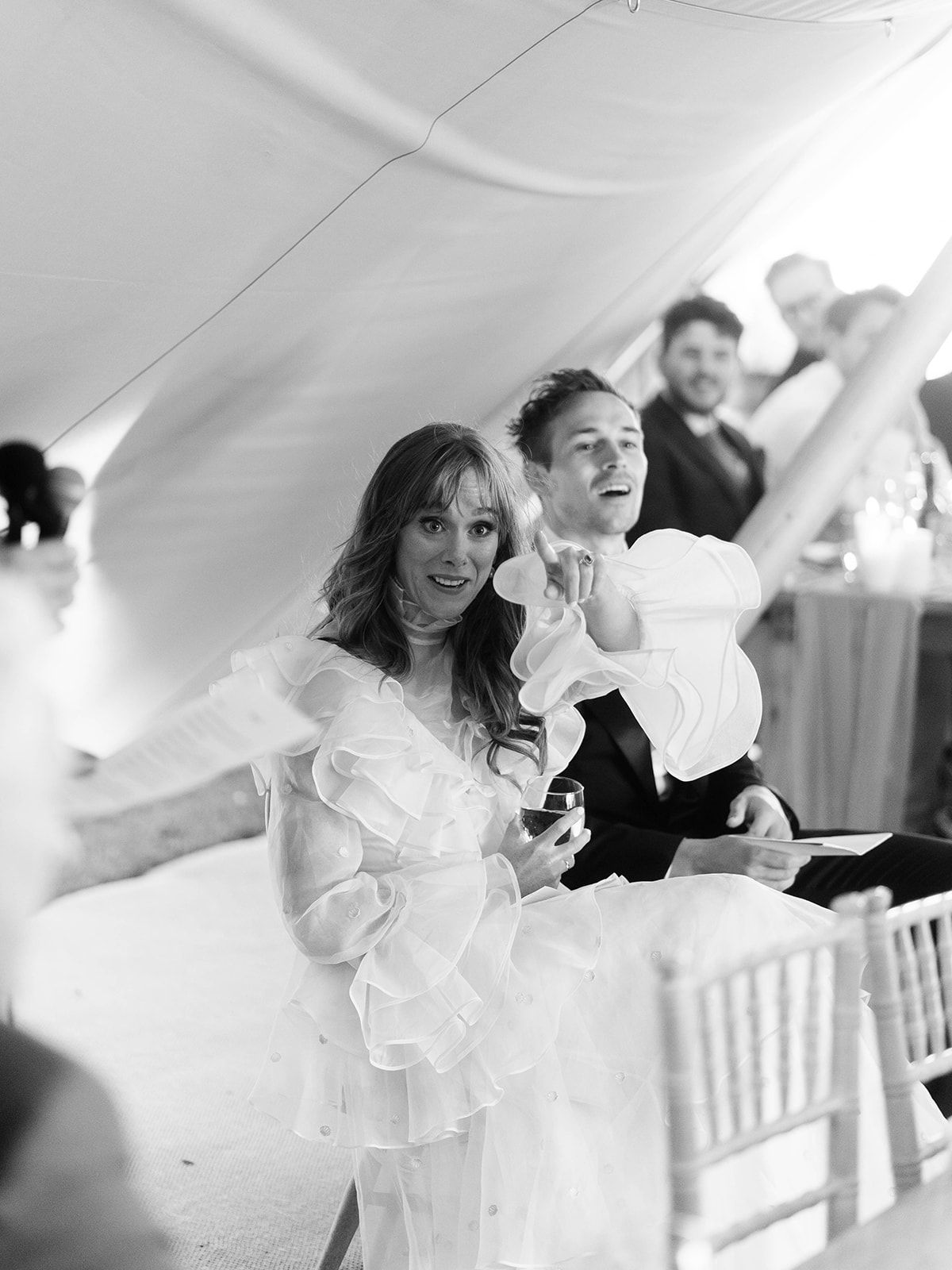 People dancing and celebrating at a wedding reception under a white tent with joyful expressions.