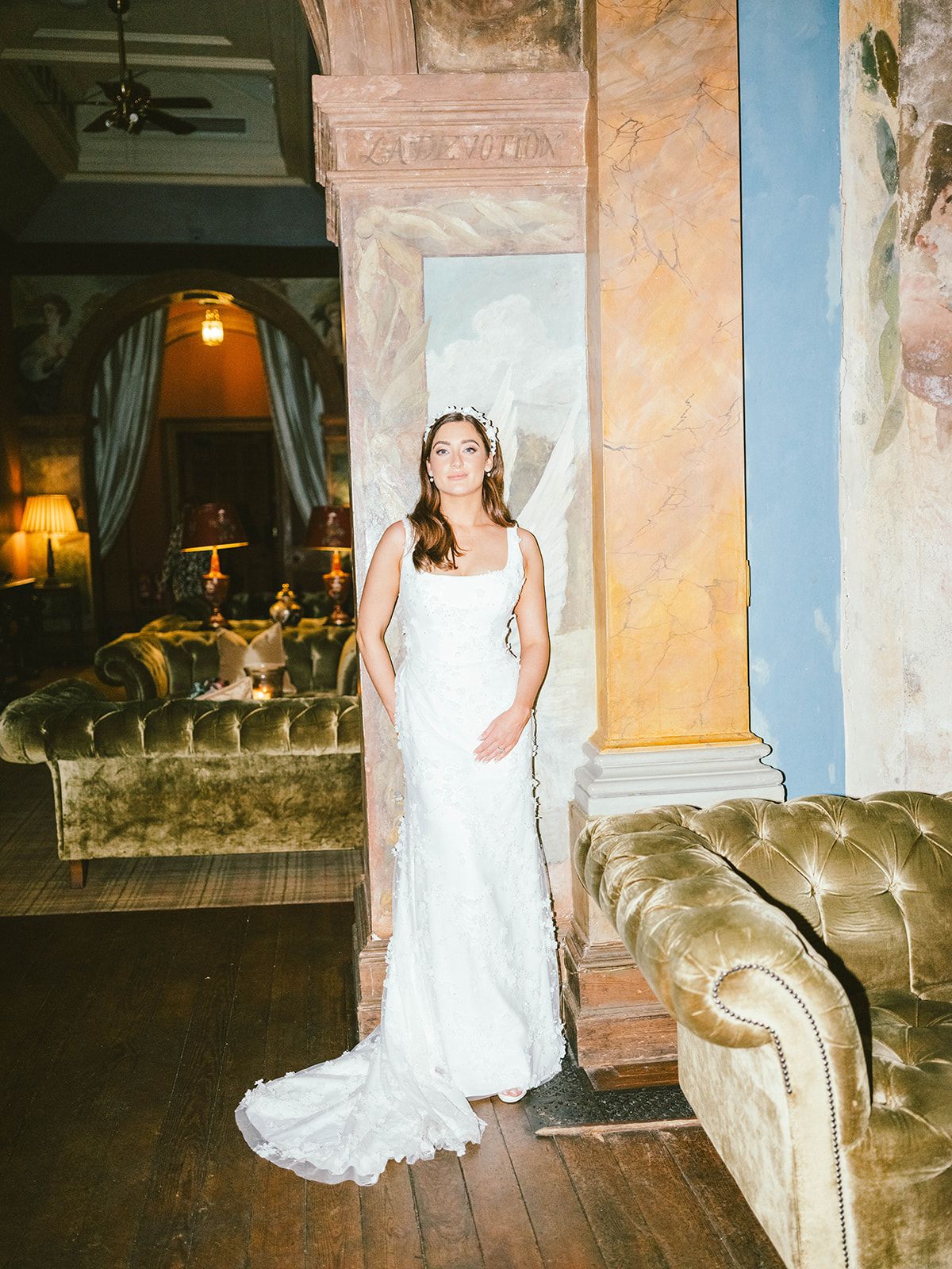 Elegant wedding dress photographed in a vintage room with ornate furnishings and warm lighting.