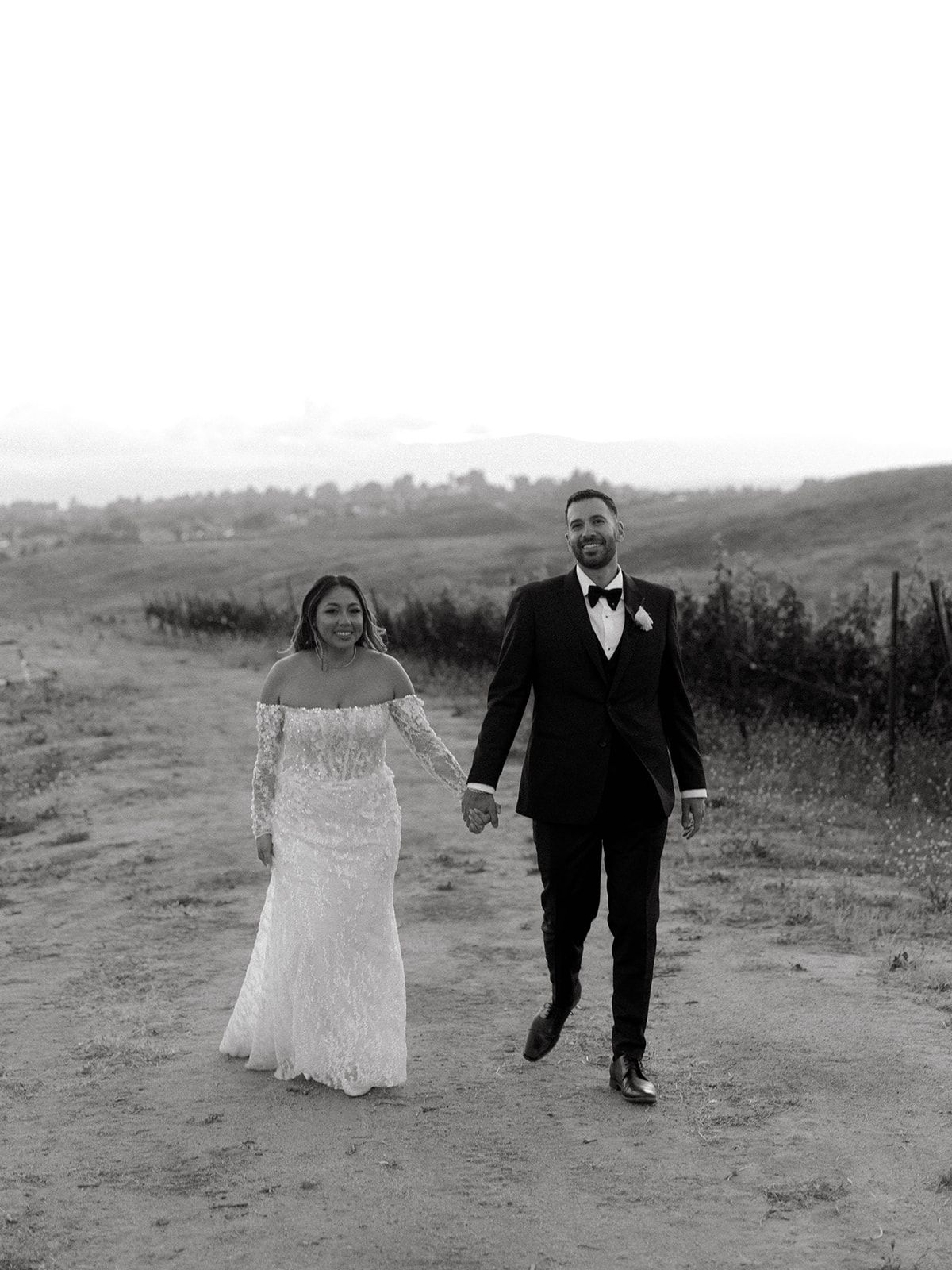 A couple walking hand in hand on a dirt path during their wedding day in black and white photography.
