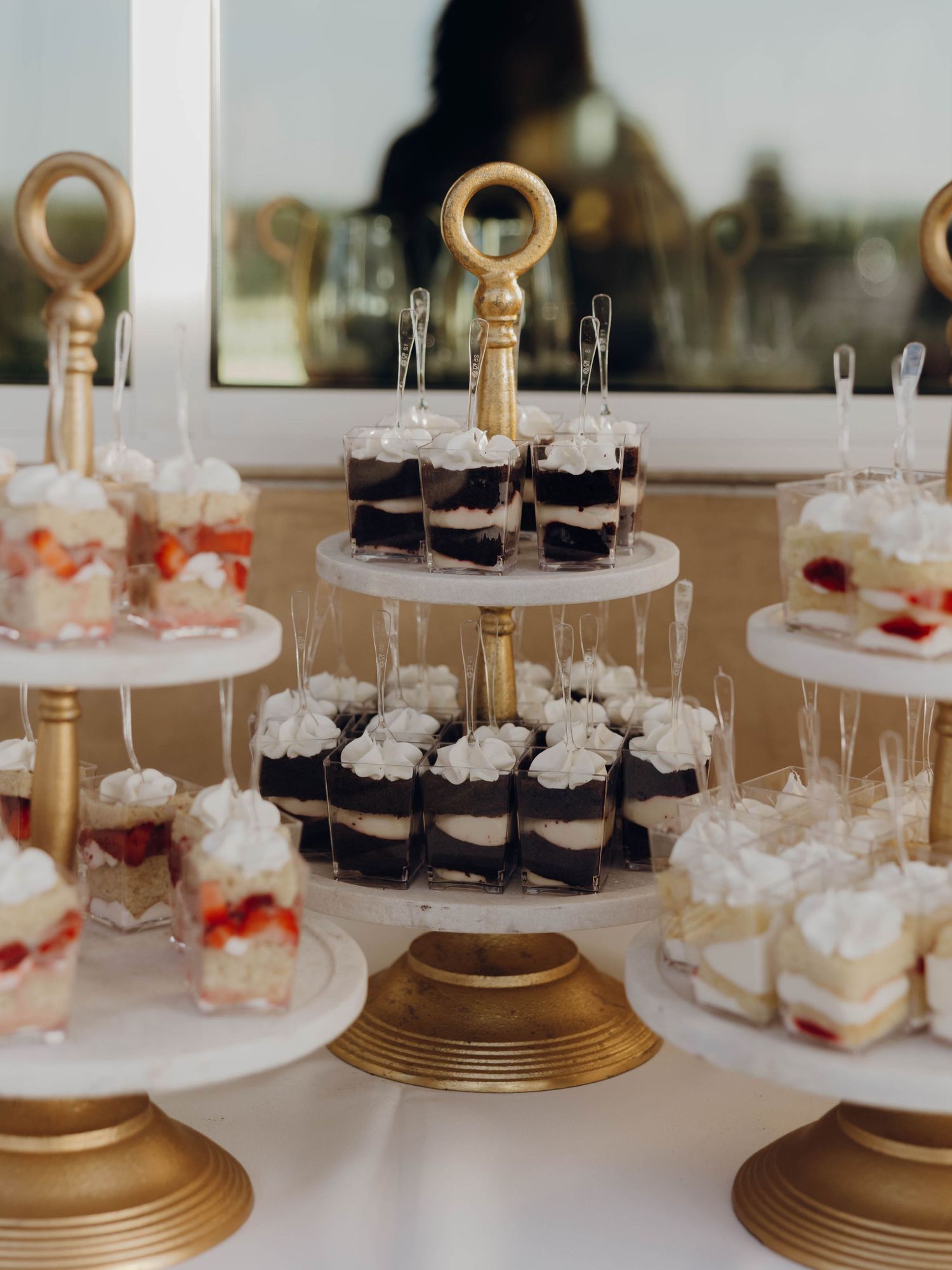 Elegant dessert display featuring tiered stands with chocolate cakes and strawberry trifles on gold pedestals.