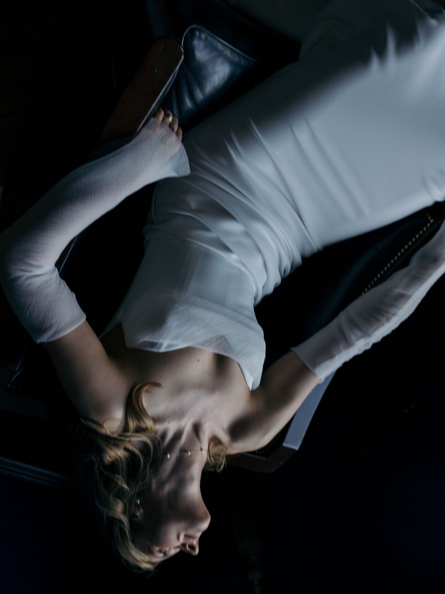 A woman in a white top lying back dramatically in dim, moody lighting with dark shadows.