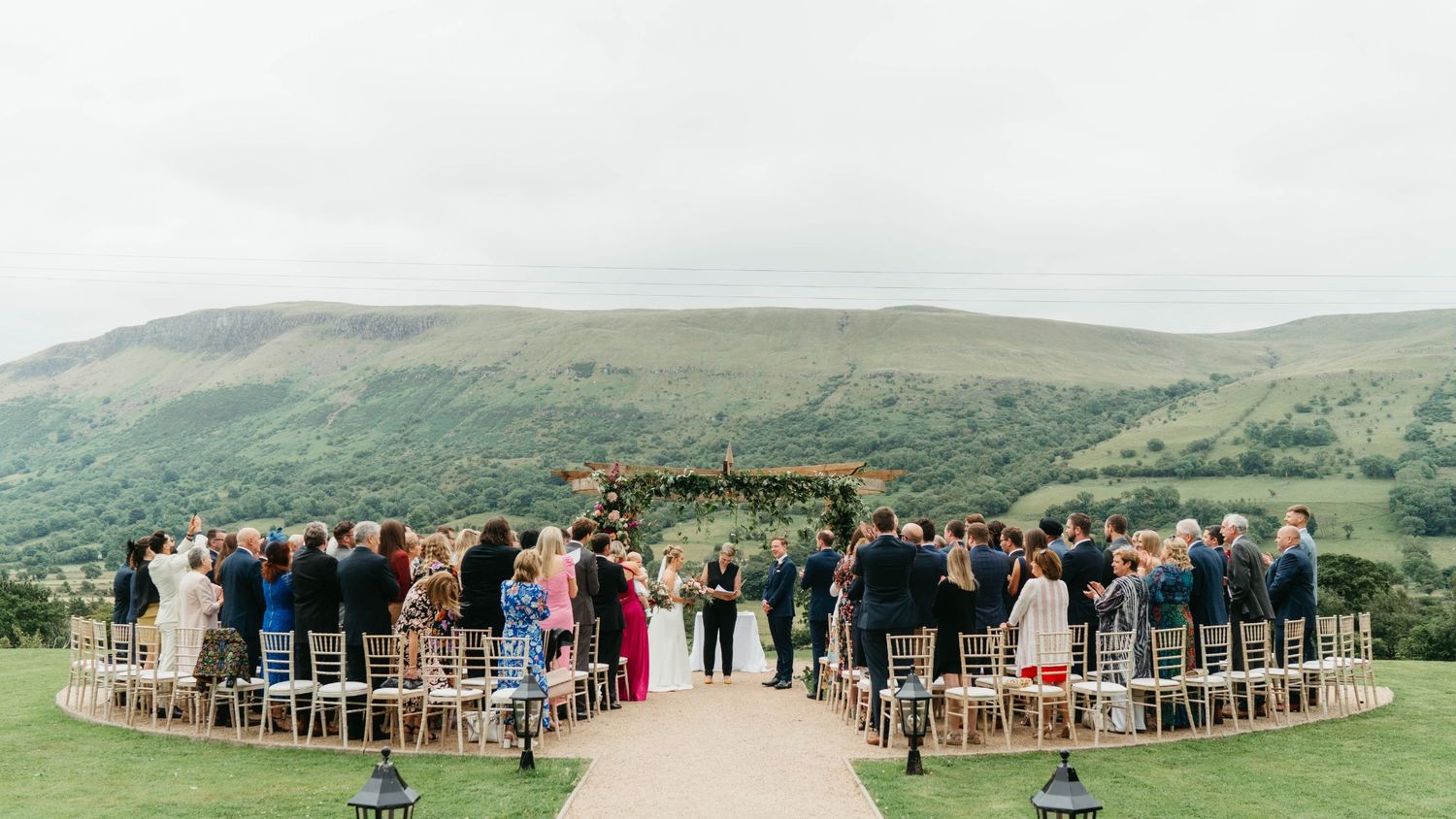 An outdoor wedding ceremony setup with rows of chairs on a hilltop overlooking green rolling mountains in the distance.