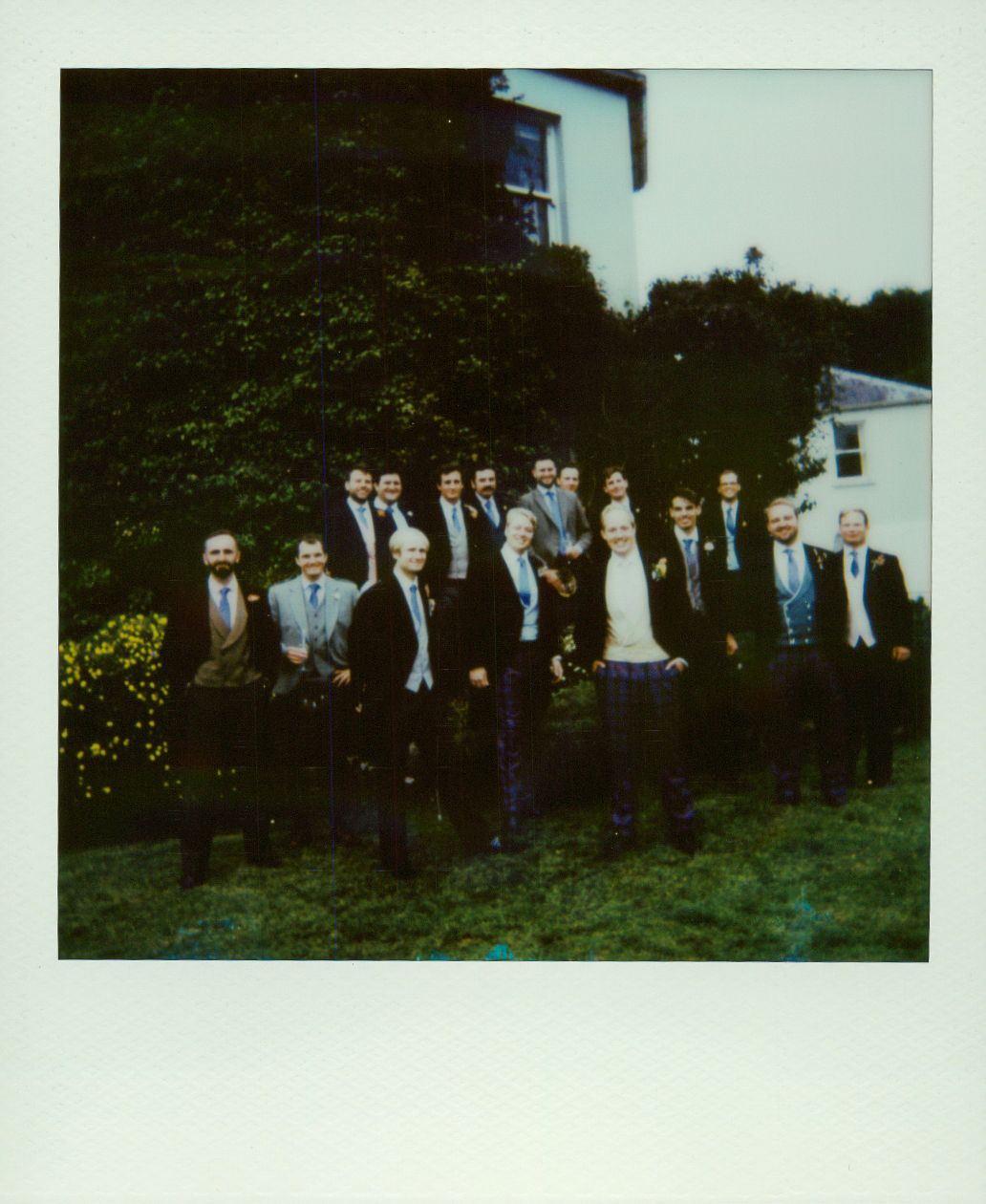 A group of formally dressed people standing together on a grassy lawn for a group photo.
