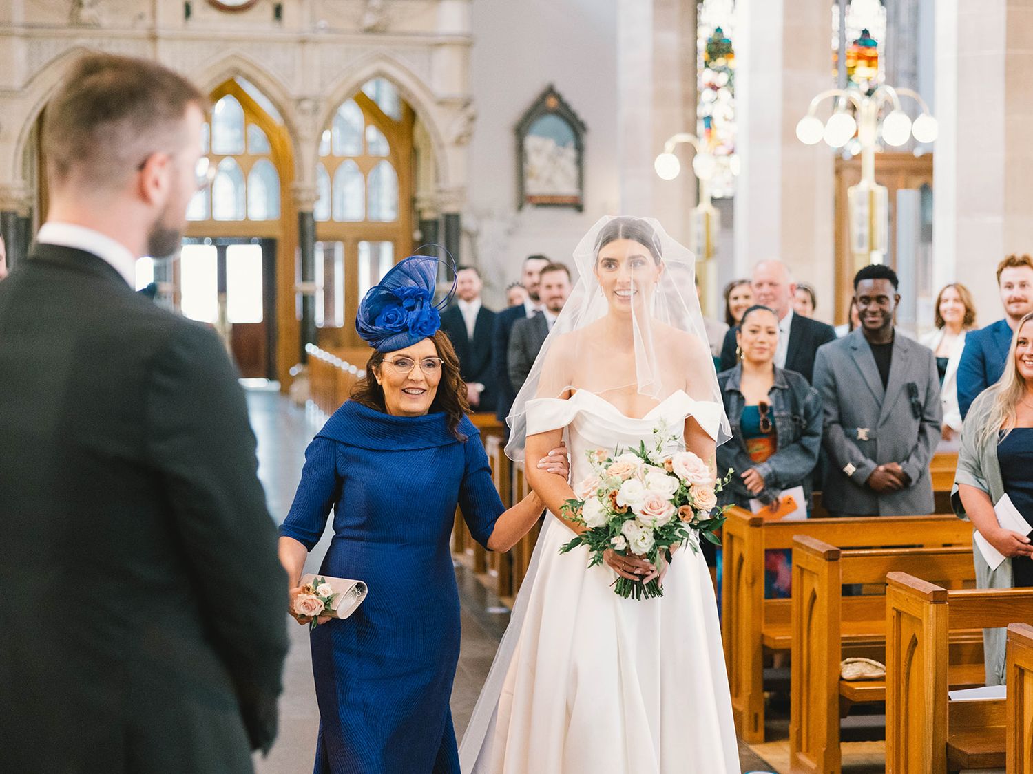 A traditional church wedding ceremony with stained glass windows and wedding guests seated in wooden pews.