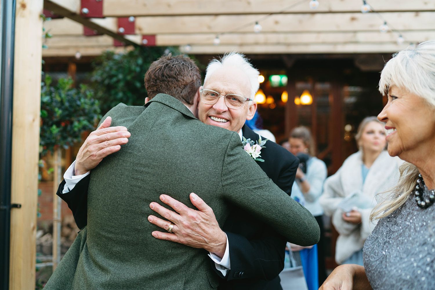 Two people share a warm embrace during an outdoor celebration with onlookers in the background.