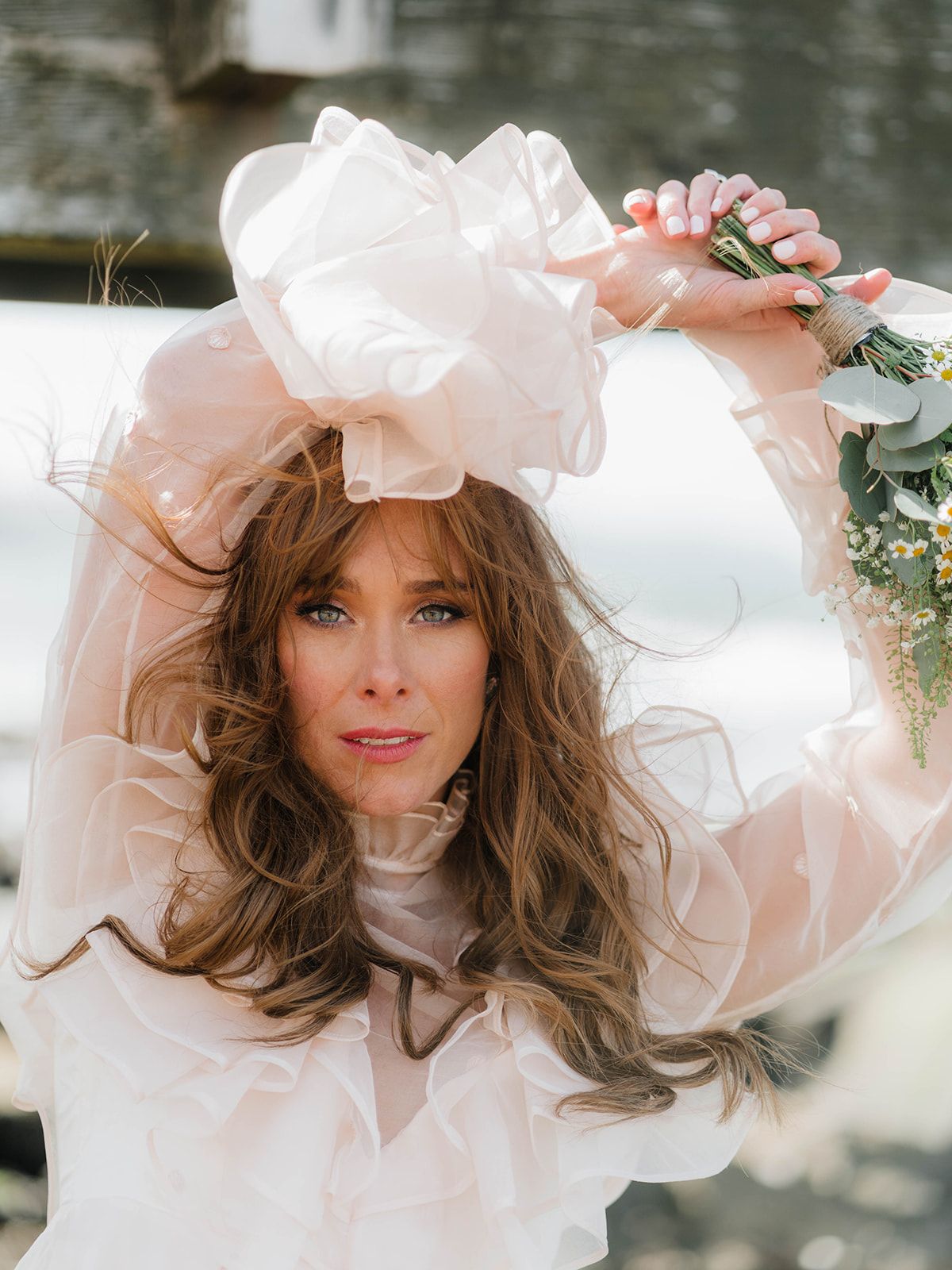 Ethereal bridal portrait featuring a flowing white dress with ruffled details and dramatic sheer sleeves in soft lighting.
