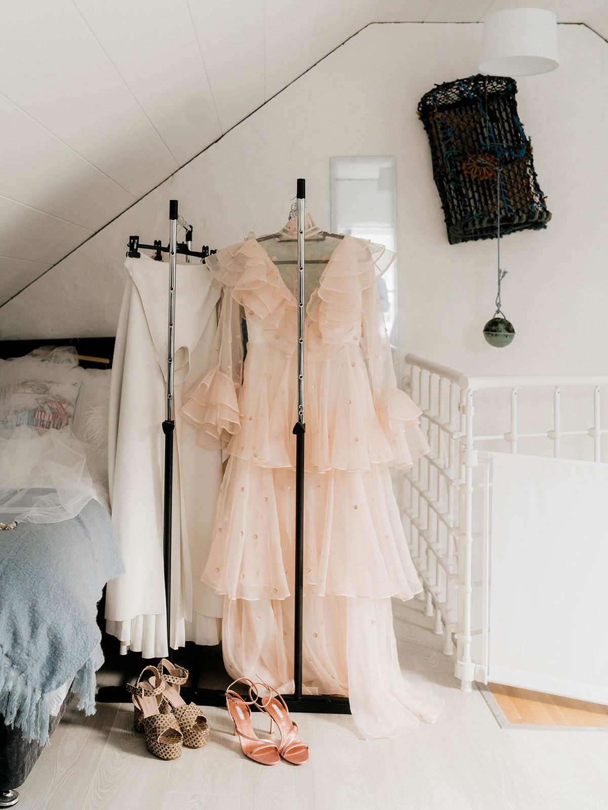 Romantic peach wedding dress displayed on rack with shoes and accessories in cozy bedroom corner.