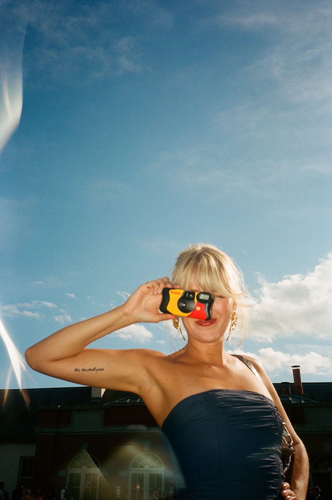 Person in black swimwear poses against bright blue sky with dramatic clouds and sunlight.