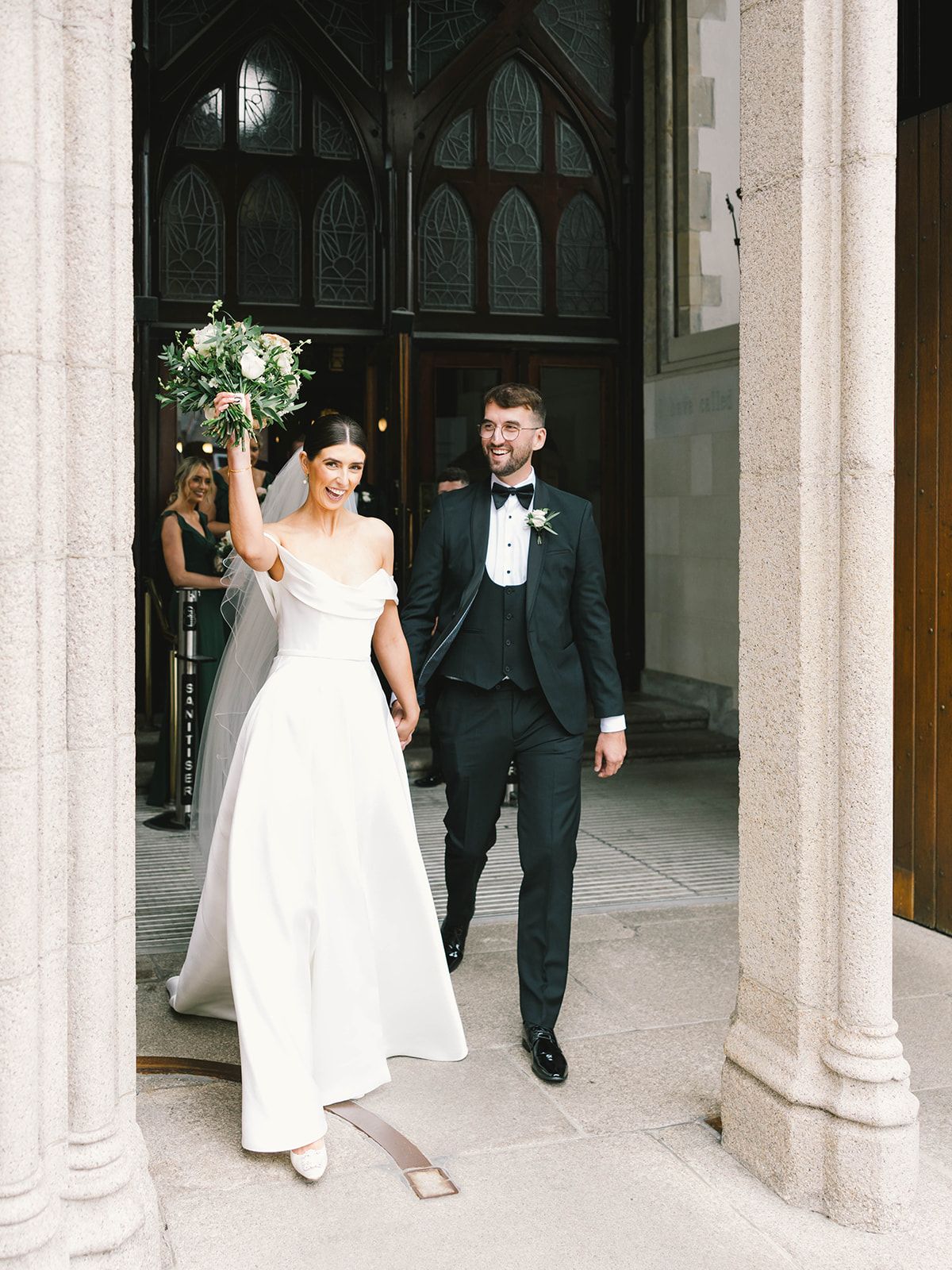 A bride and groom exit a gothic church doorway with stone columns and arched architectural details.
