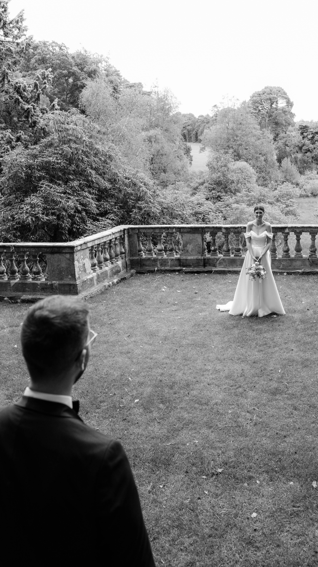 Black and white outdoor wedding photo on a garden terrace with stone balustrade.