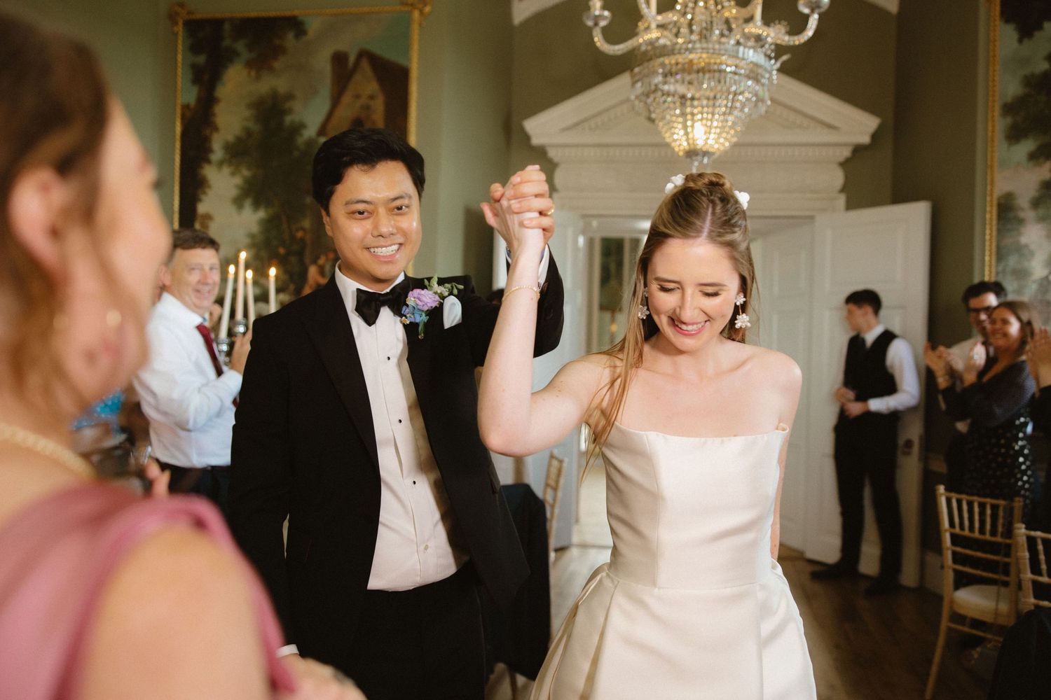 A newlywed couple celebrating with raised arms during their wedding reception in an elegant ballroom.