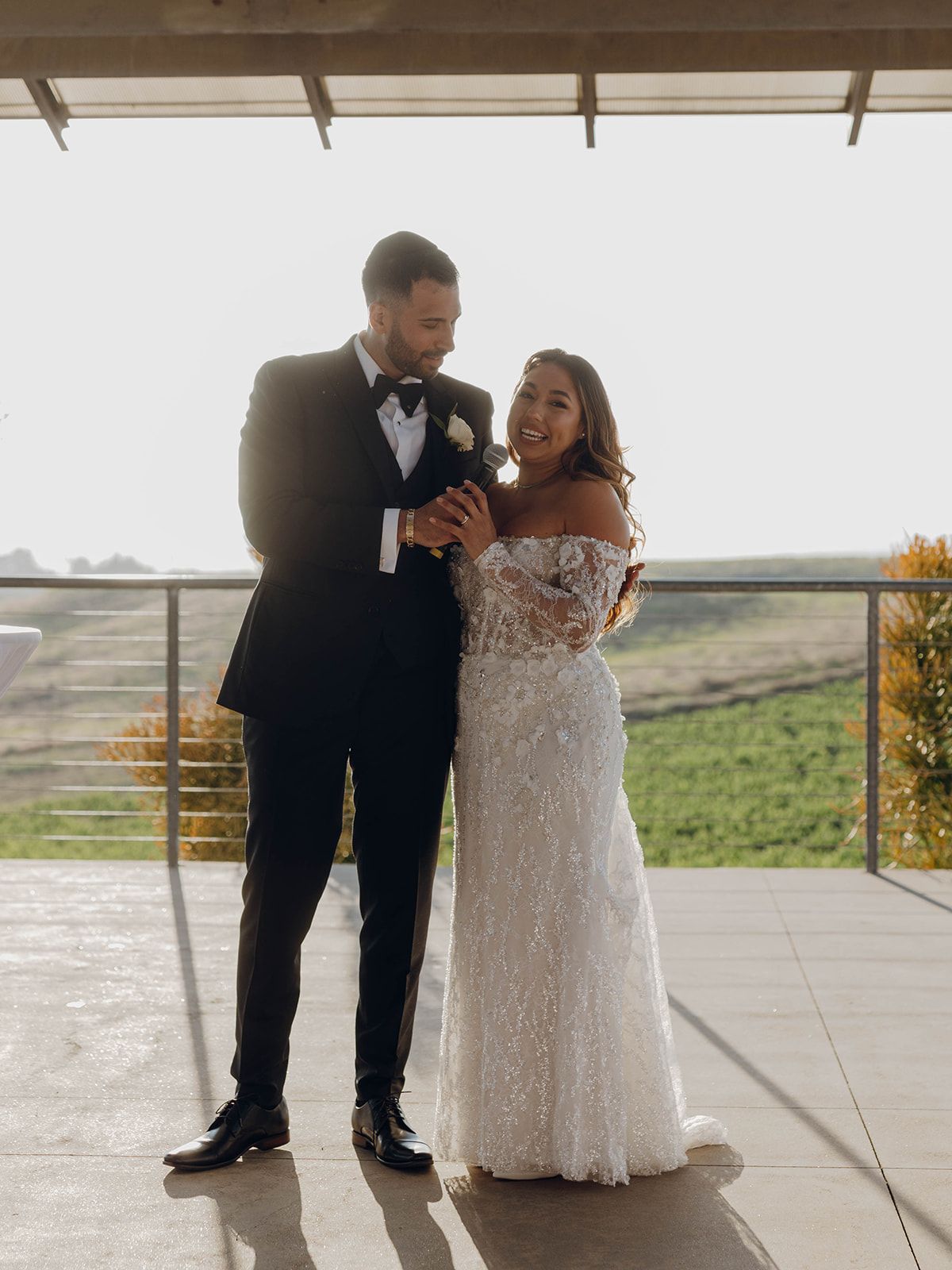 A couple shares a candid moment of laughter on their wedding day at a scenic outdoor venue.