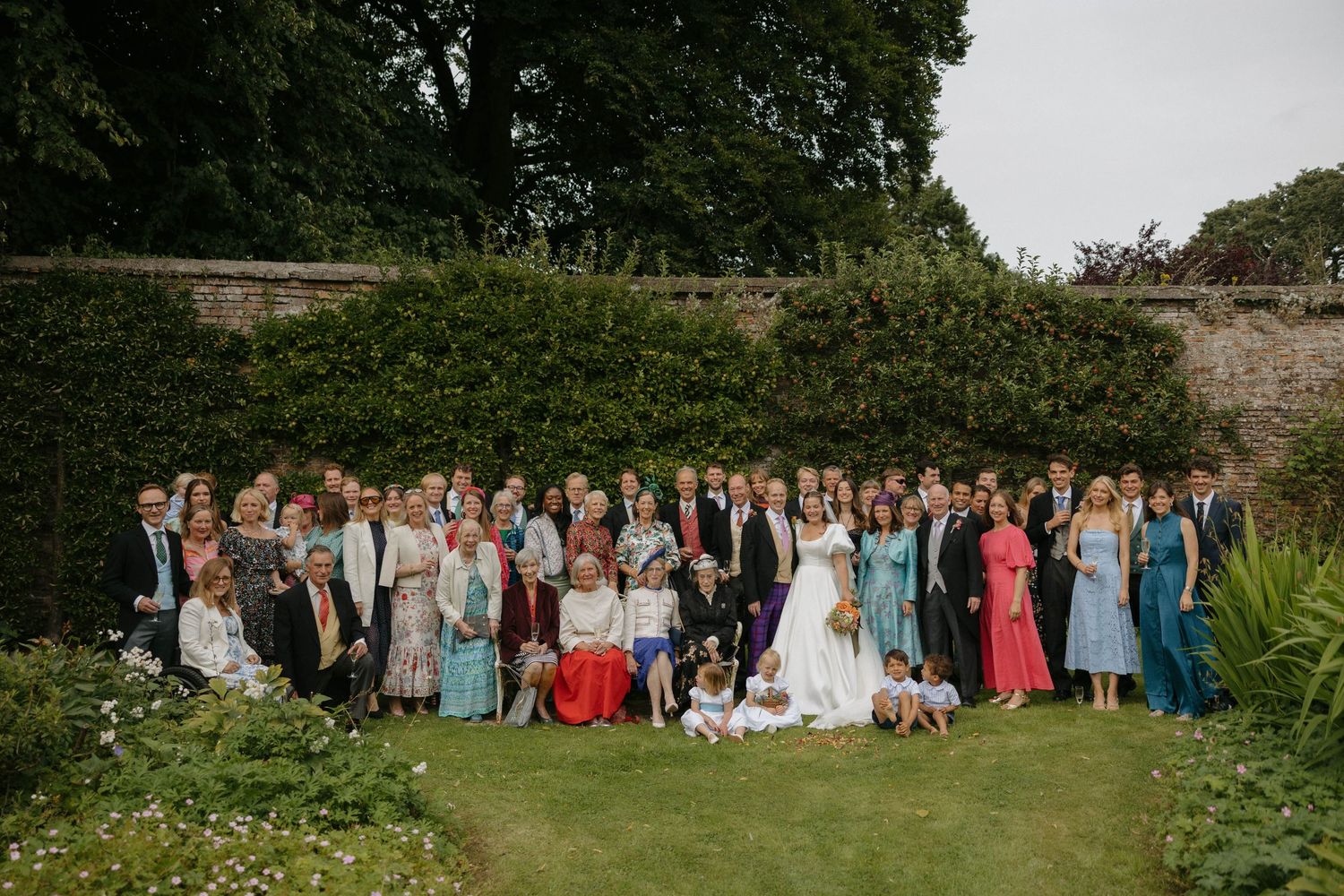 A panoramic sequence of outdoor group photos showing wedding guests in formal attire gathered in a garden setting.