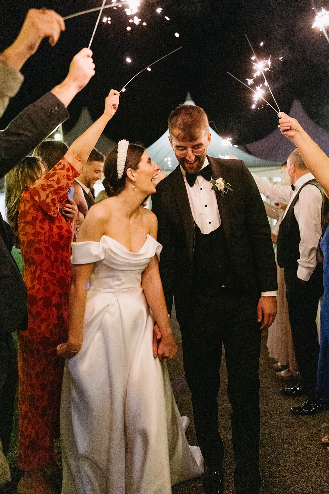 A couple in wedding attire share a joyous moment under sparklers during their outdoor nighttime celebration.