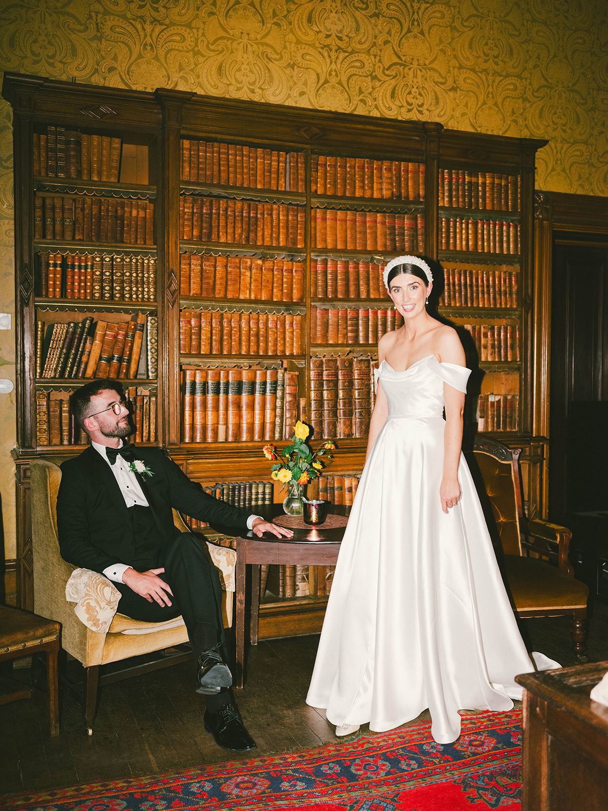 A wedding scene in an elegant wood-paneled library with floor-to-ceiling bookshelves, traditional furnishings and a Persian rug.