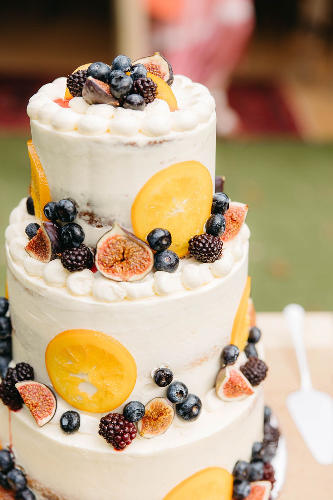 A white wedding cake decorated with fresh citrus slices, blueberries, blackberries and figs in a rustic style.