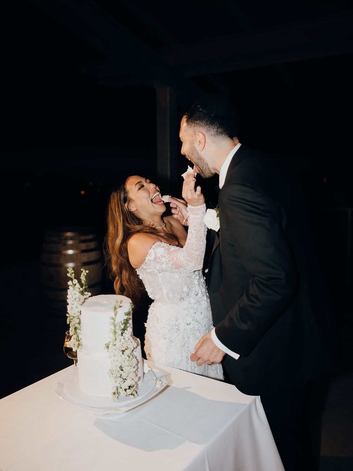A romantic moment between newlyweds sharing their wedding cake at a dimly lit reception.