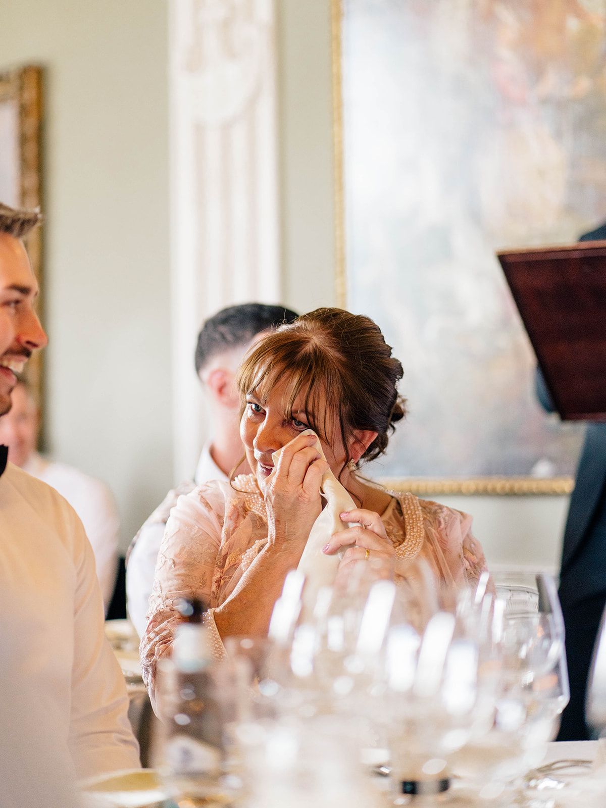 An emotional moment captured during a wedding reception as someone wipes away tears while seated at an elegant dinner table.
