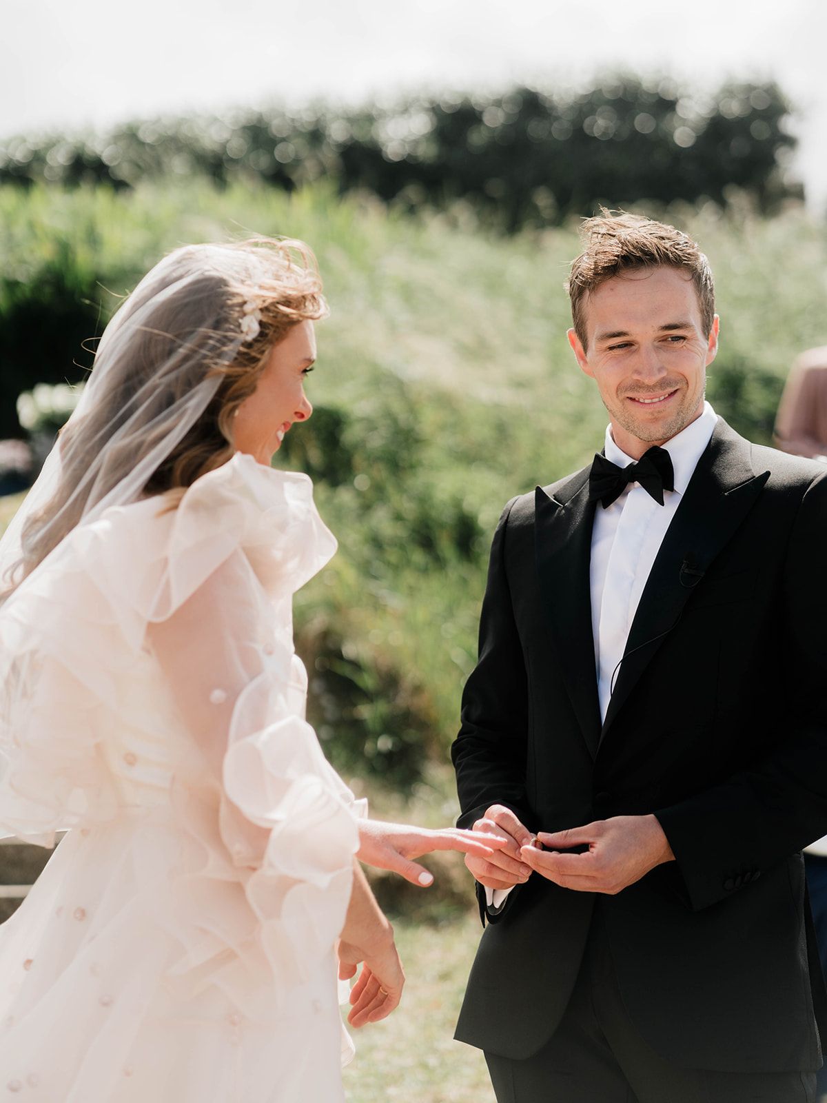 Newlyweds share a tender moment during their wedding ring exchange in a sunlit garden setting.