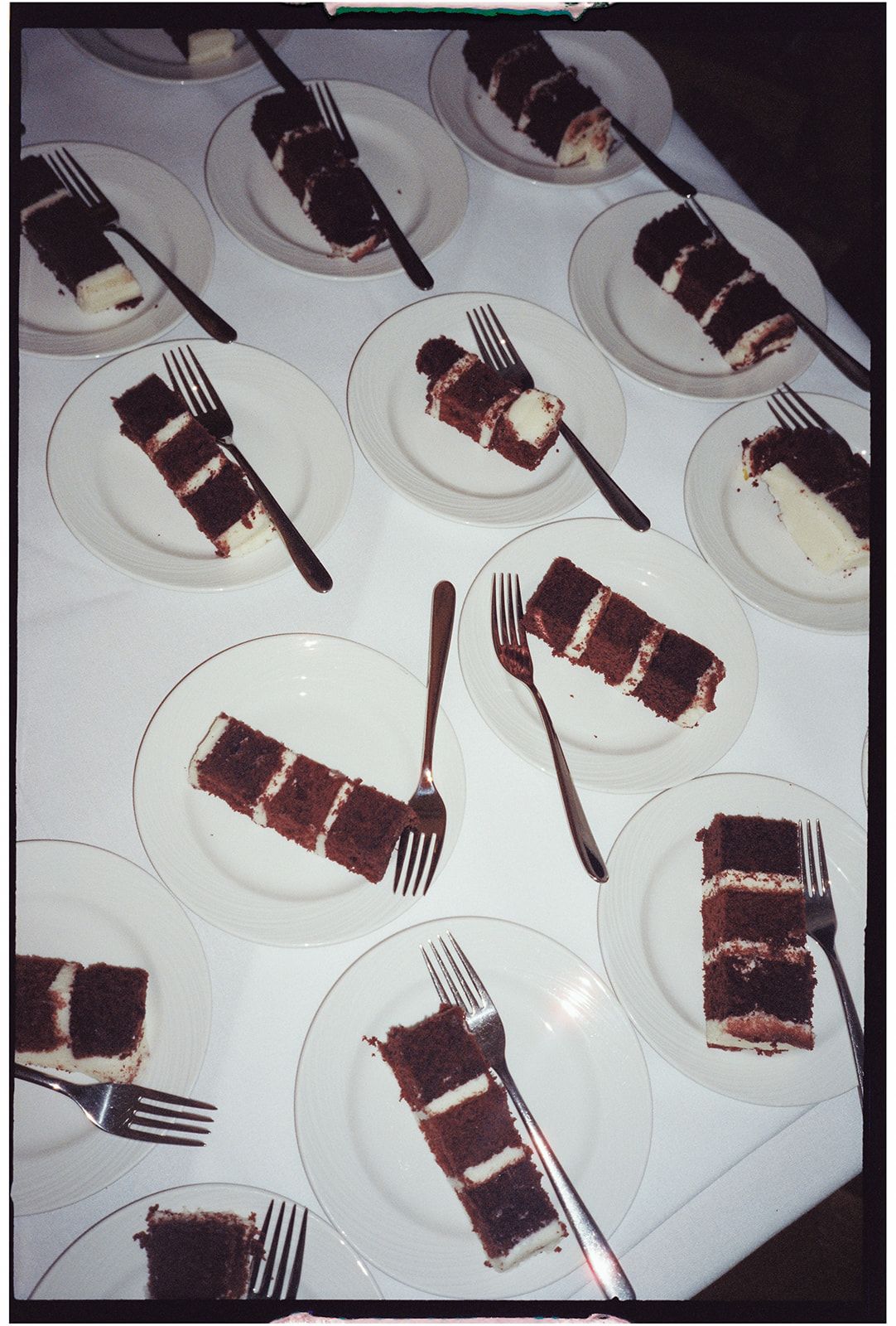 Multiple plates of layered chocolate cake slices with cream filling arranged in rows on a white surface.