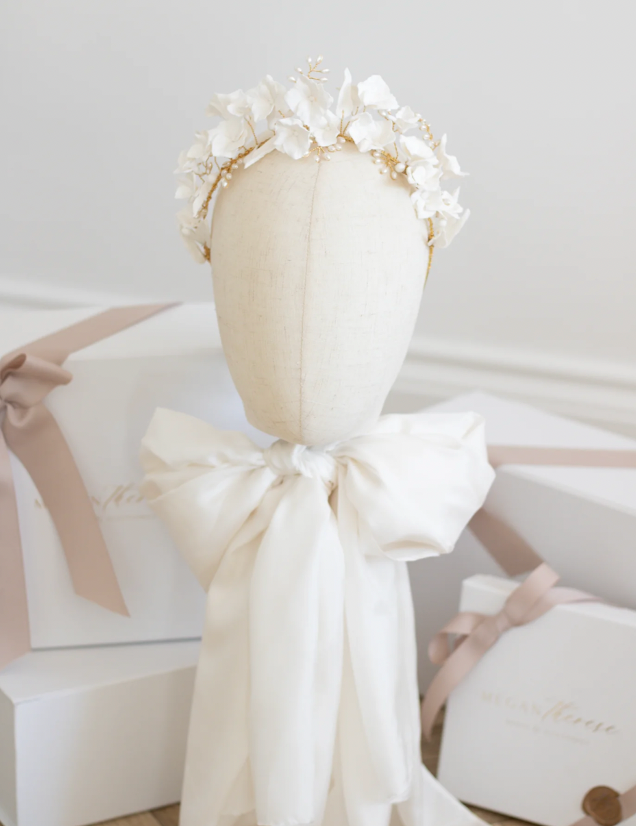 Elegant white dress with delicate bow details and floral accents displayed in a soft, ethereal setting.