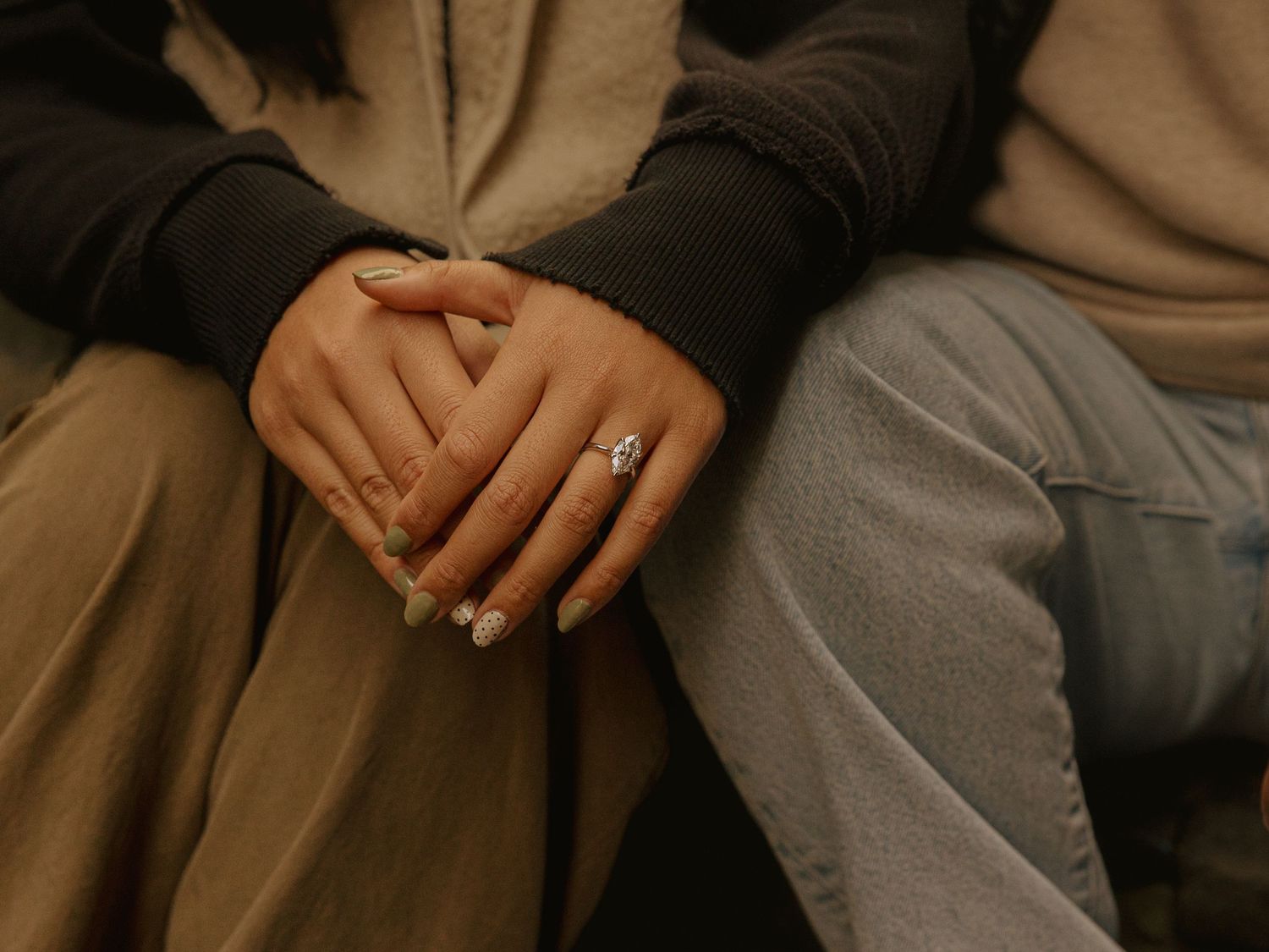 Close-up of hands with engagement ring resting on neutral fabric.
