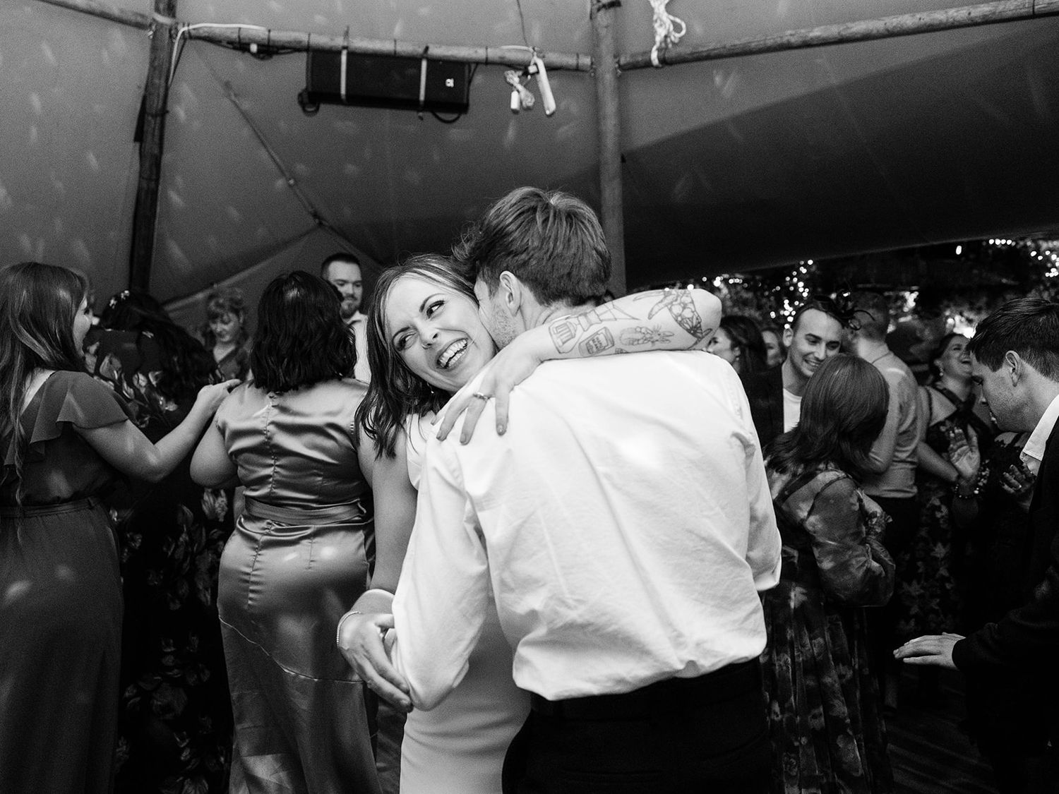Black and white photo of couples dancing at a lively wedding reception party under a tent.
